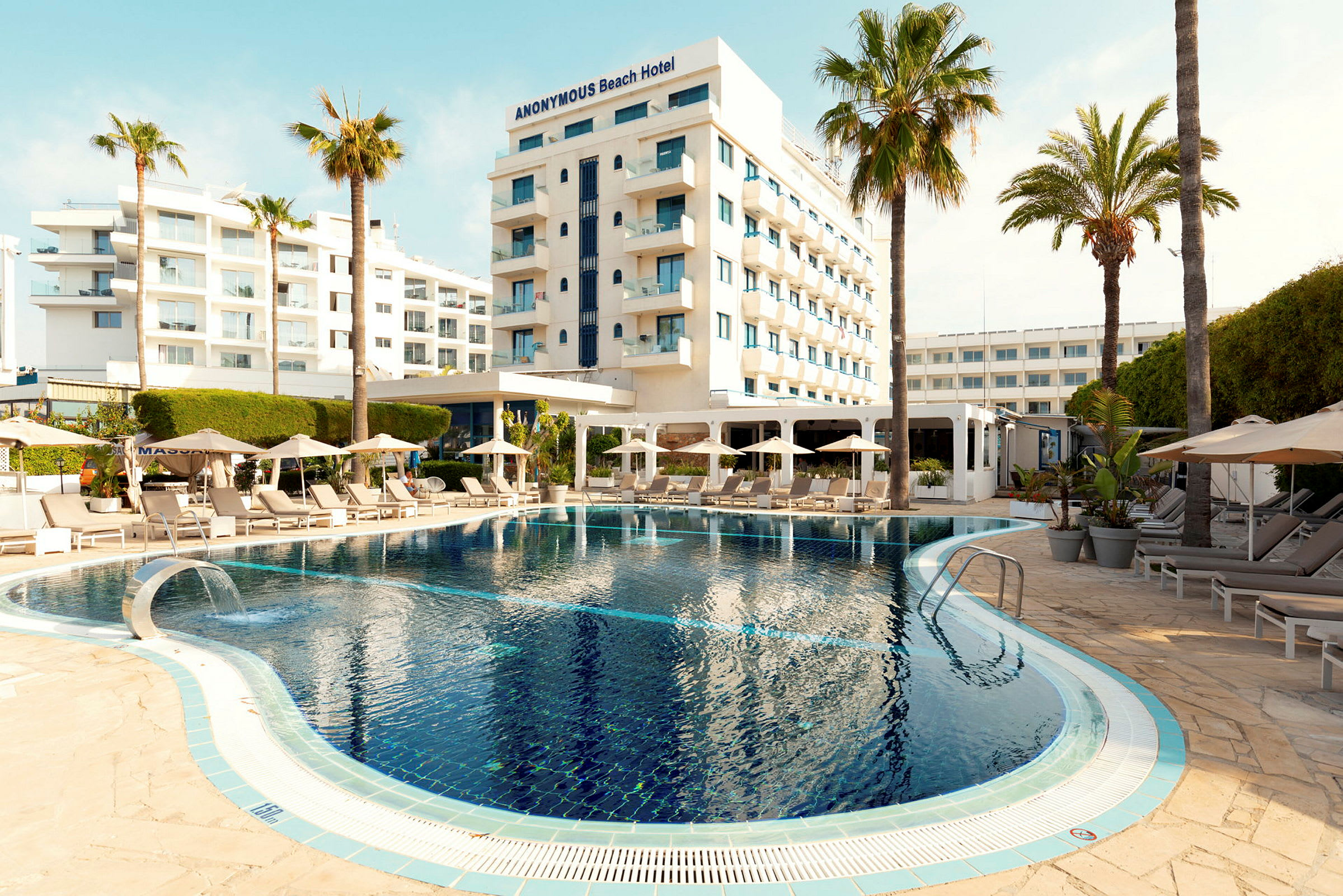 Hotelbygning med pool og solsenge omgivet af palmer. (AI-genereret tekst)