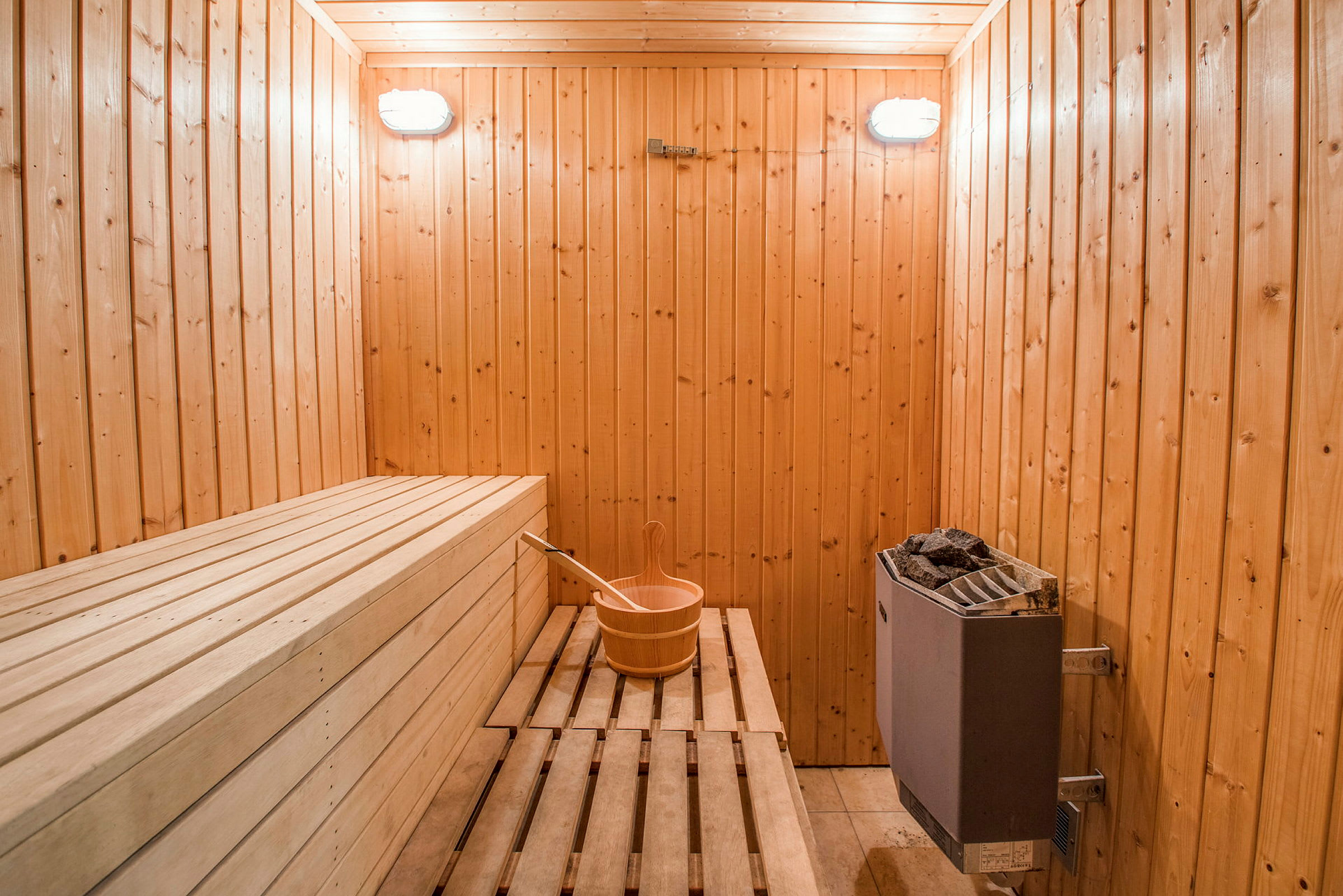 En sauna med træpaneler, bænke, en spand med ske og en saunaovn. (AI-genereret tekst)
