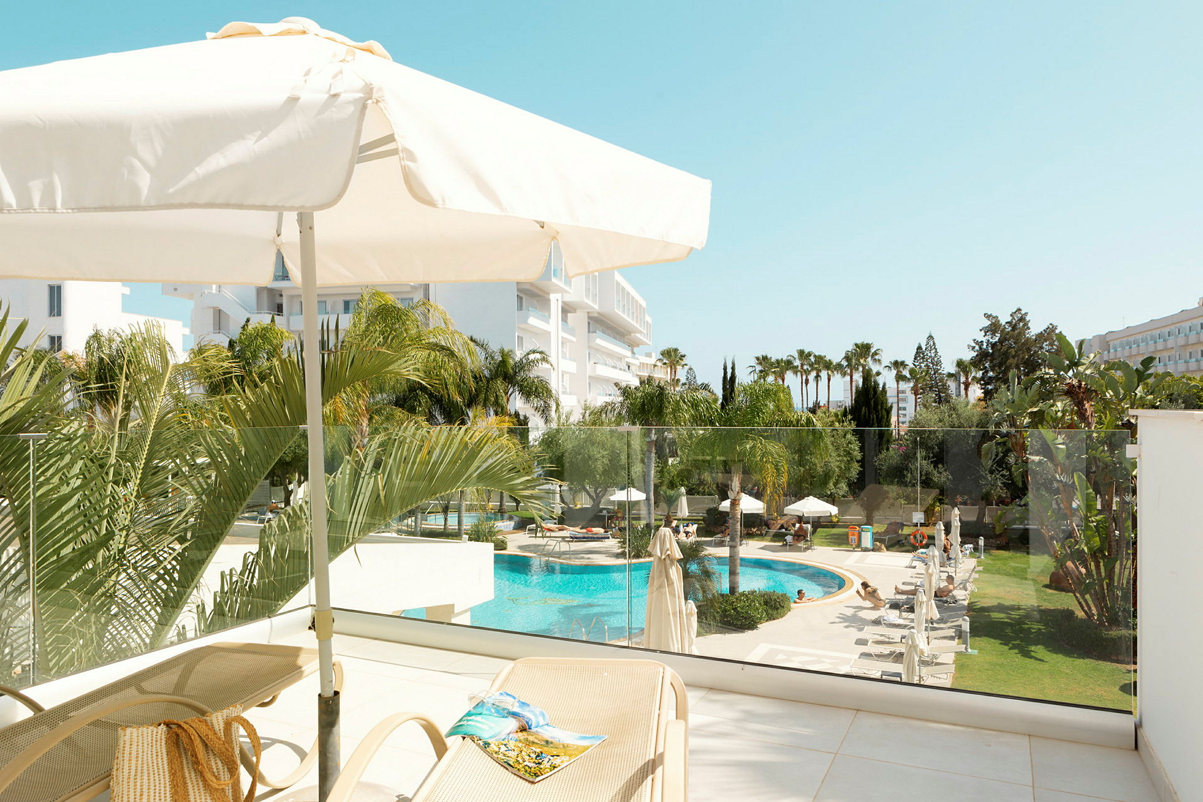 Udsigt fra en terrasse med parasol, liggestole og udsigt over en pool og have. (AI-genereret tekst)