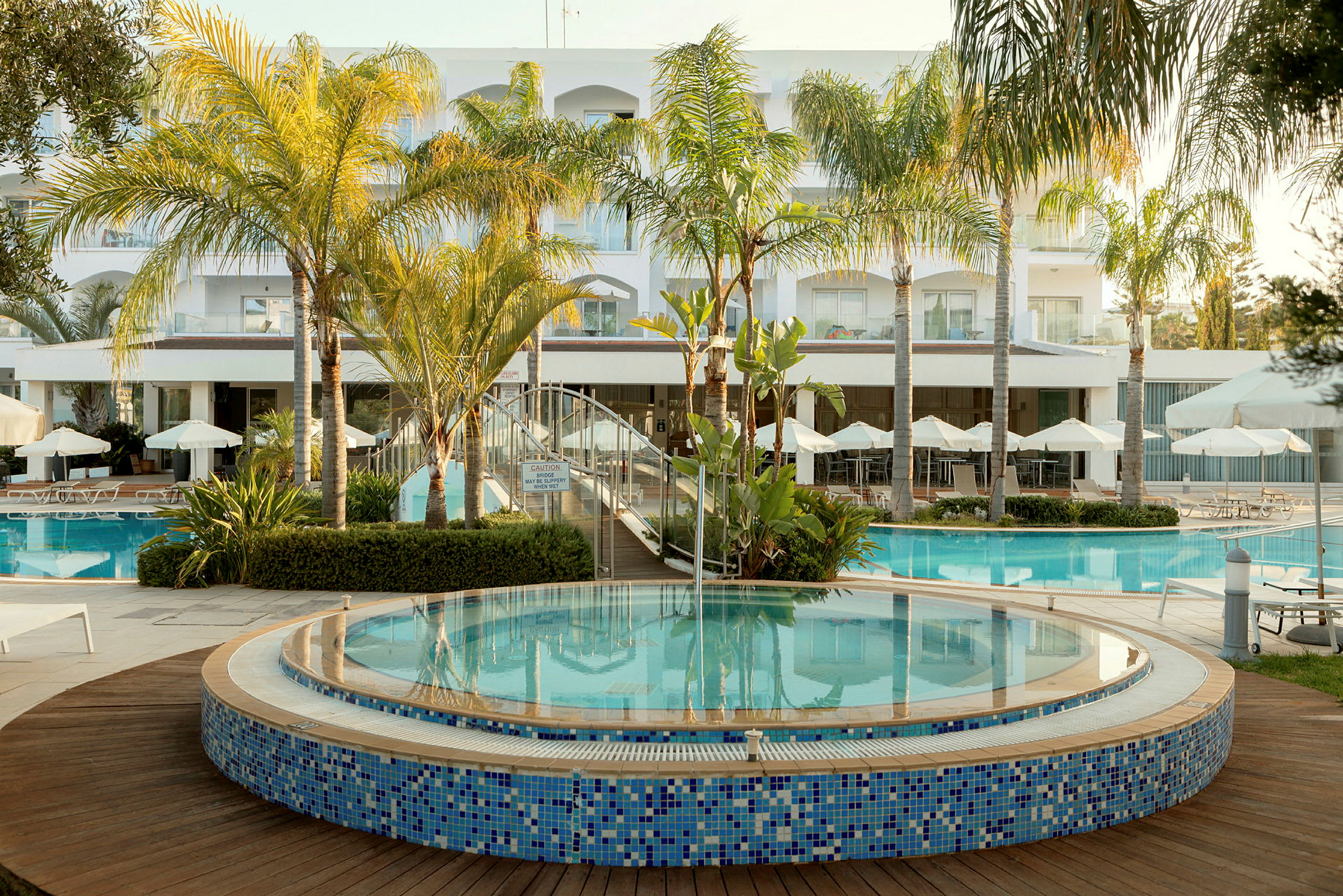 Et moderne hotel med en pool omgivet af palmer og liggestole. (AI-genereret tekst)
