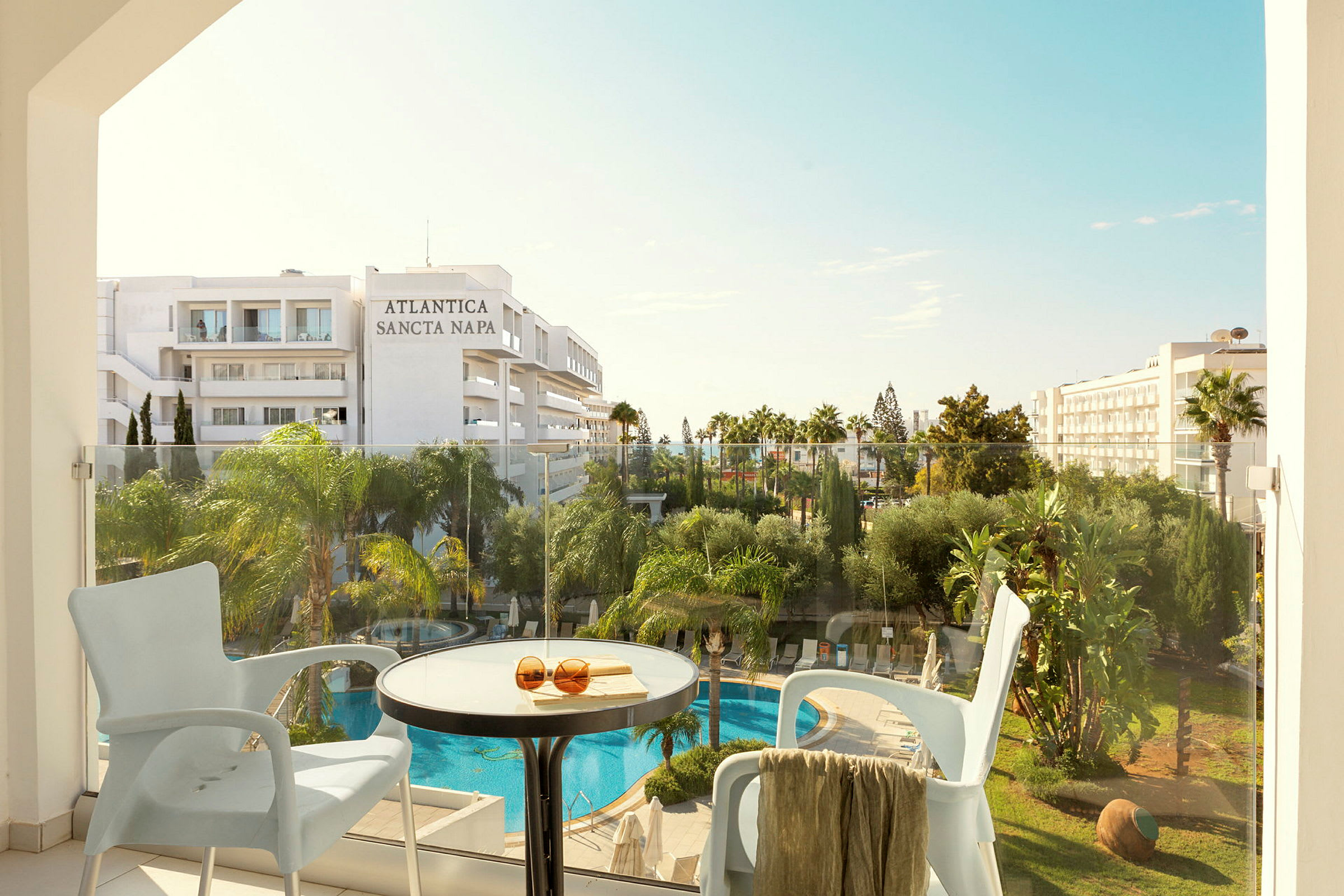 Udsigt fra en balkon mod et hotel med en pool og grønne planter. (AI-genereret tekst)