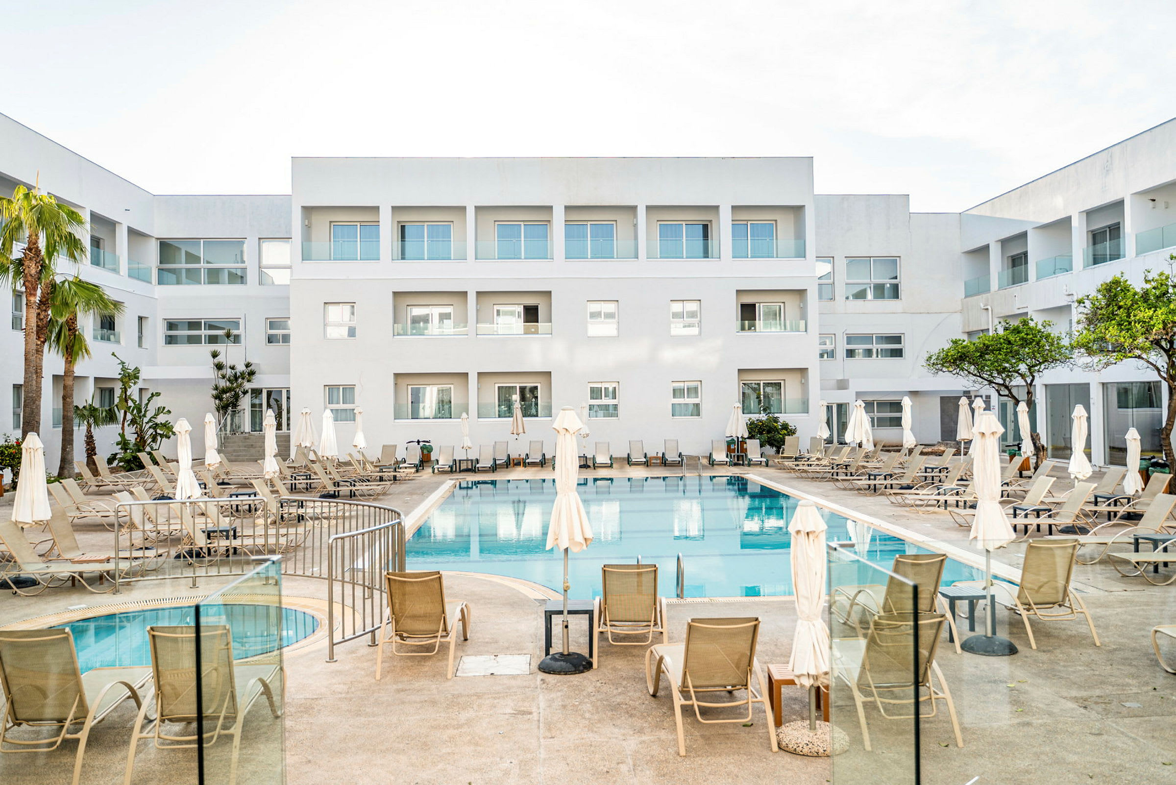 Et hotel med en udendørs pool og liggestole, omgivet af hvide bygninger. (AI-genereret tekst)