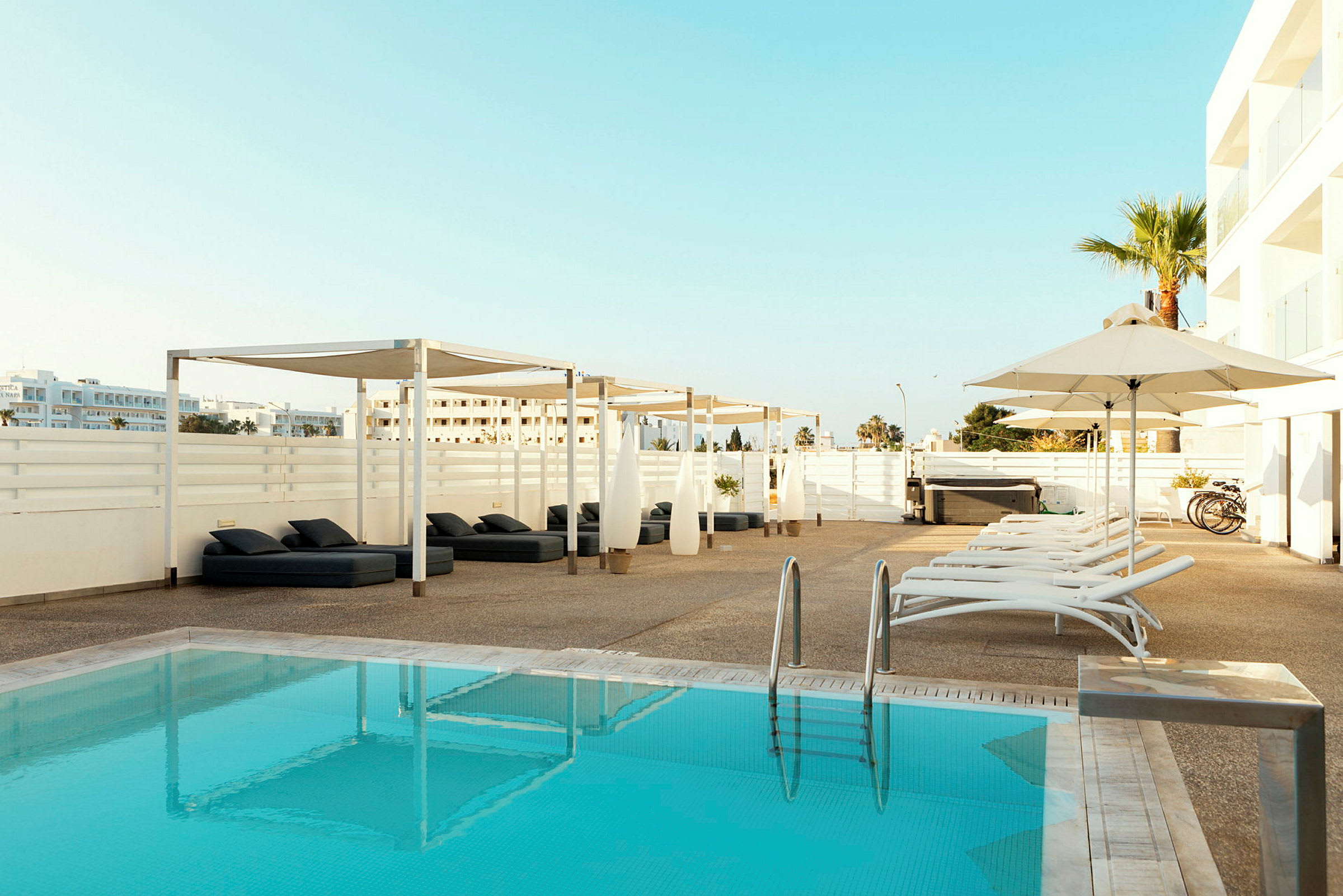 Udendørs pool med liggestole, pergola og parasoller omkring. (AI-genereret tekst)