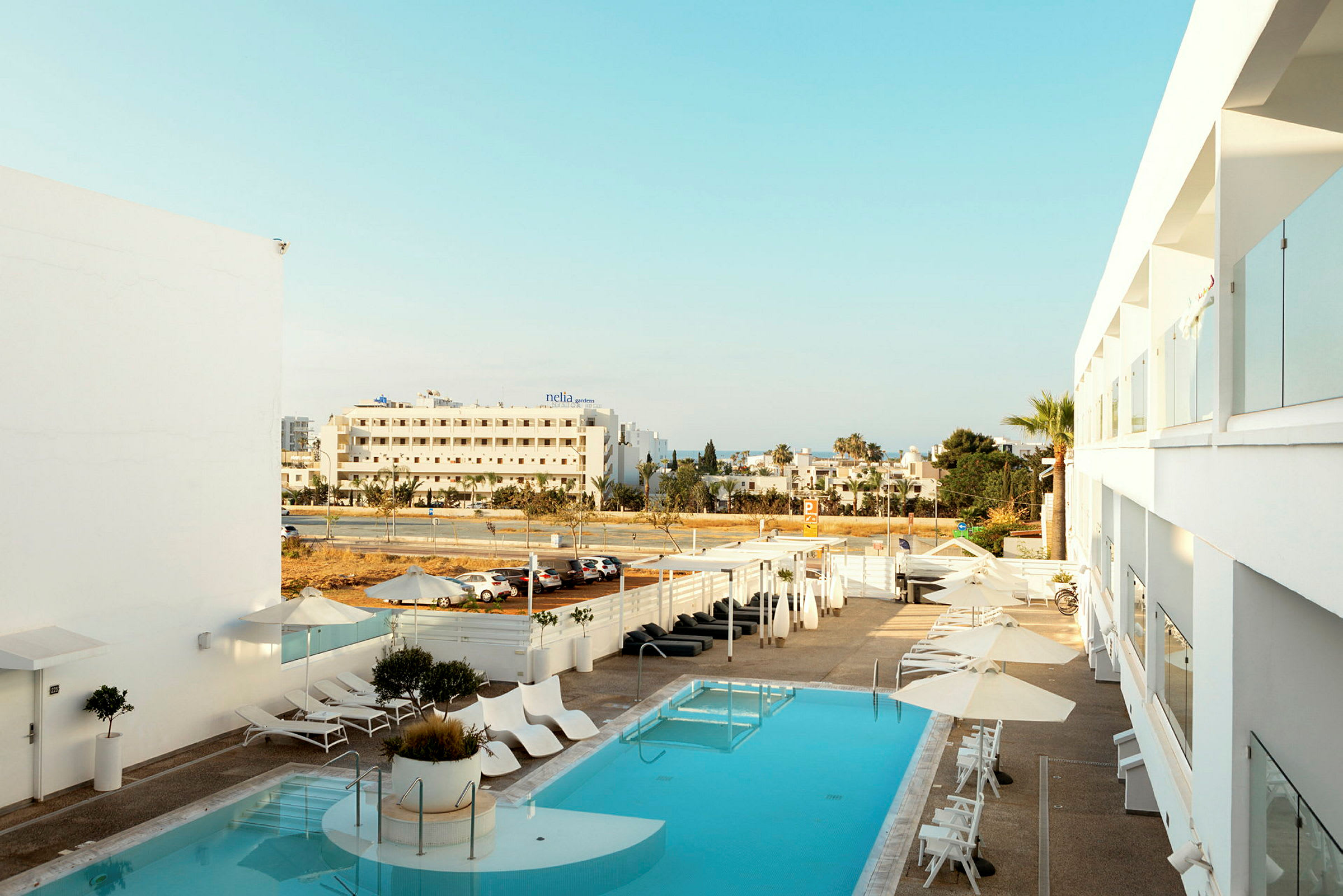 Hotel pool med liggestole og parasoller, udsigt til gaden og de omkringliggende bygninger. (AI-genereret tekst)