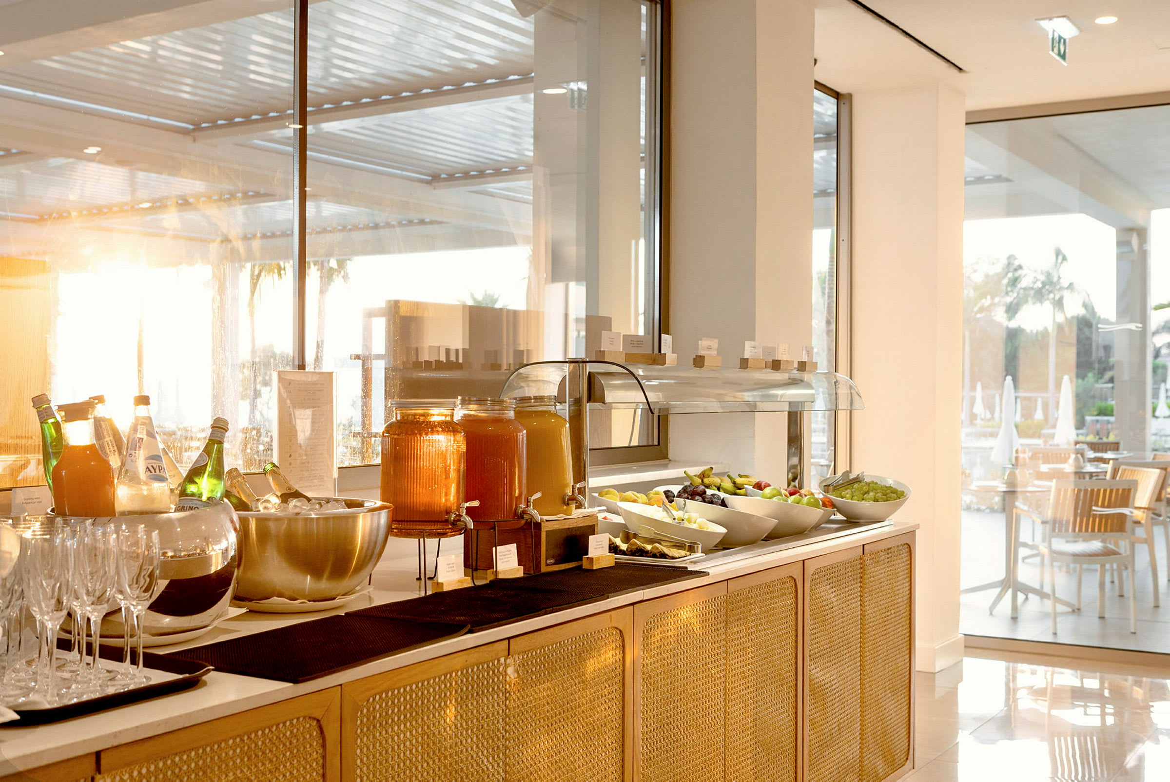 Buffet med køkkenudstyr, juice og frisk frugt i et lyst lokale. (AI-genereret tekst)