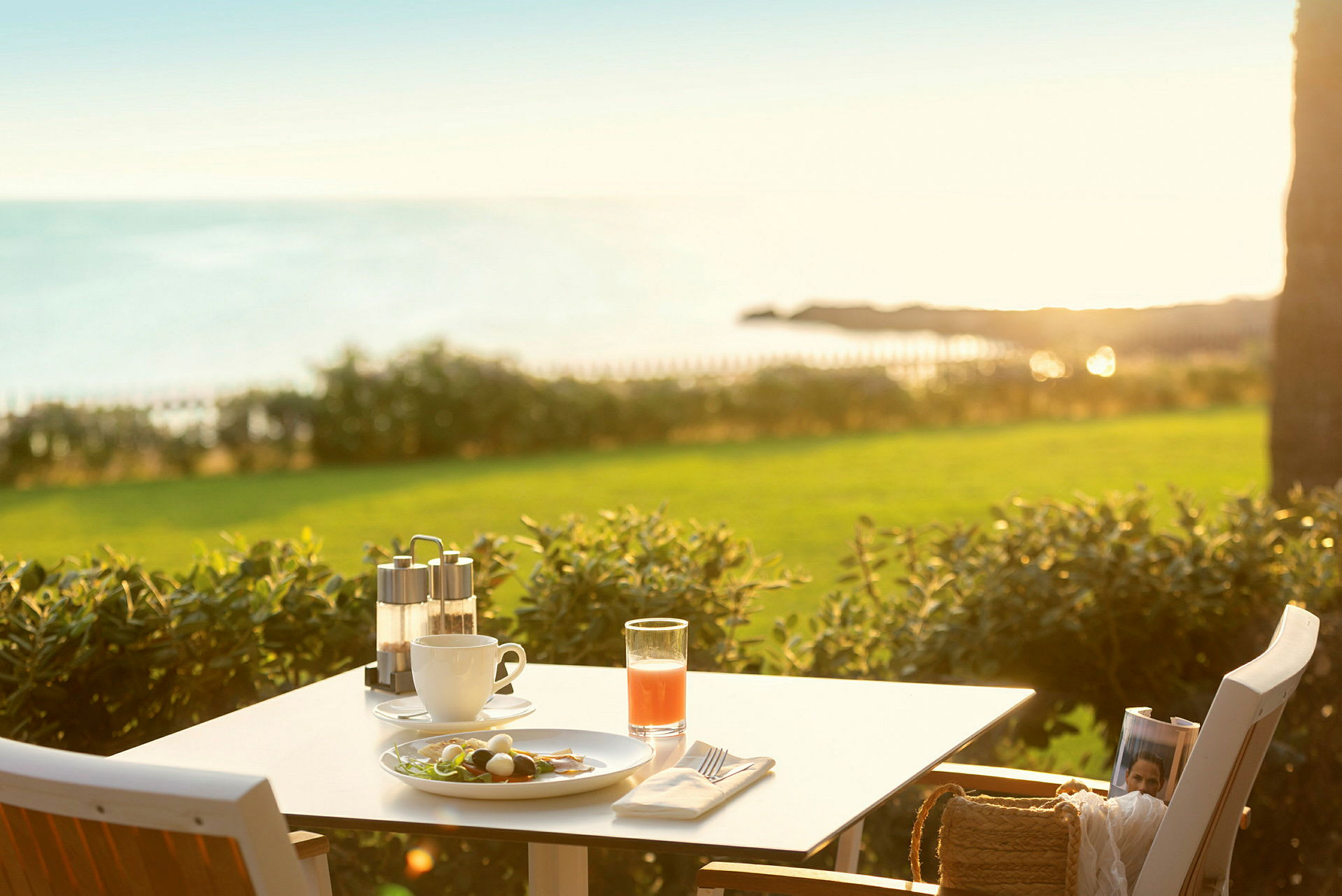 Et bord med morgenmad mod en solrig udsigt over havet og grønne områder. (AI-genereret tekst)
