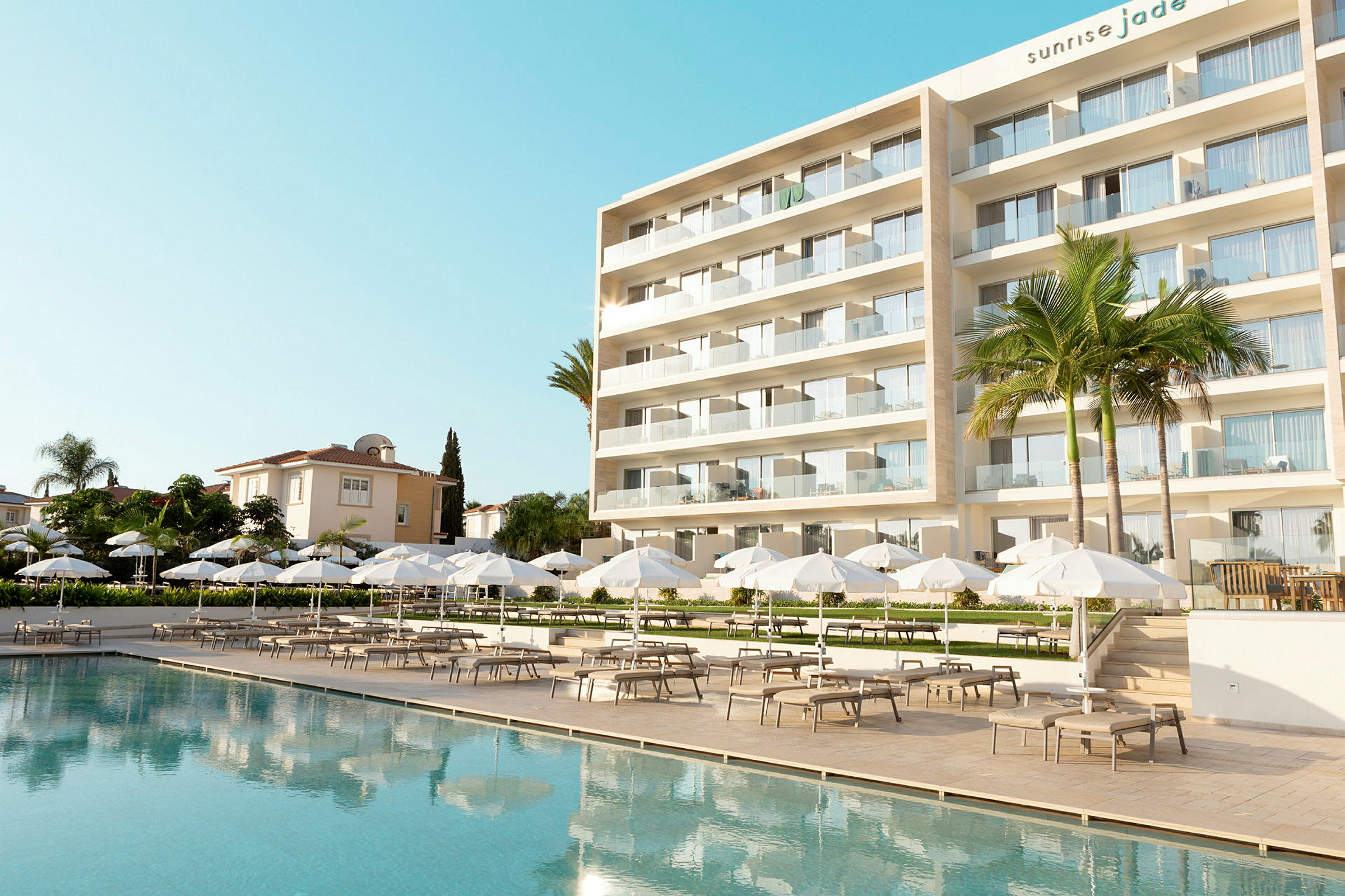 Moderne hotel med en stor udendørs pool, hvide parasoller og liggestole. (AI-genereret tekst)