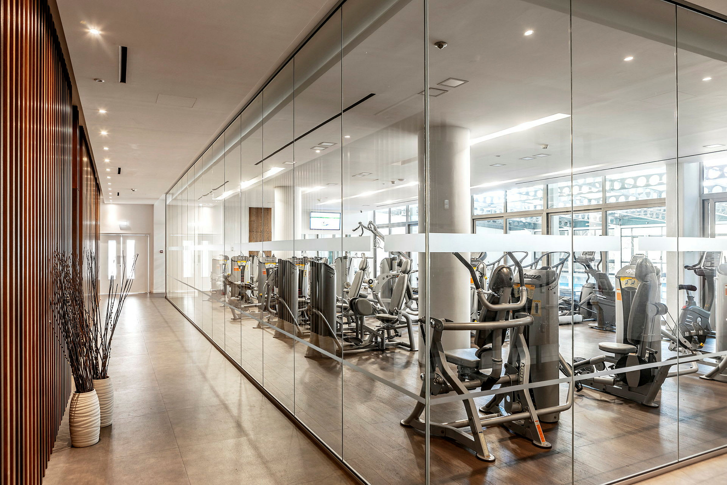 Moderne fitnessrum med træningsmaskiner bag glasvæg. (AI-genereret tekst)