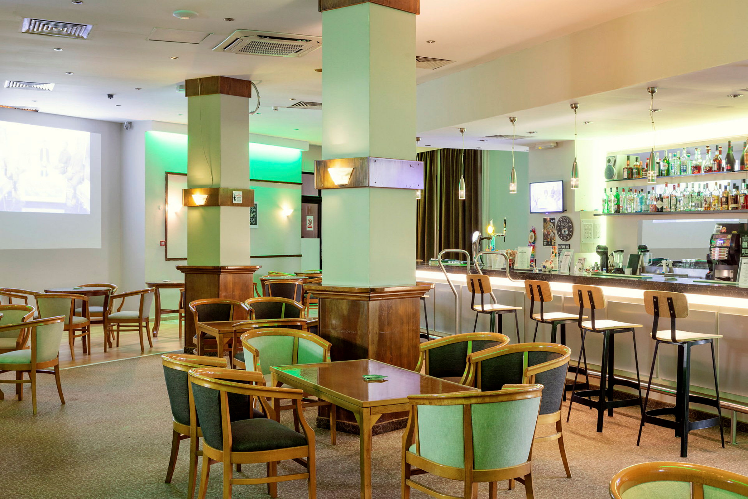En hotelbar med siddepladser og borde samt hylder med flasker bag bardisken. (AI-genereret tekst)