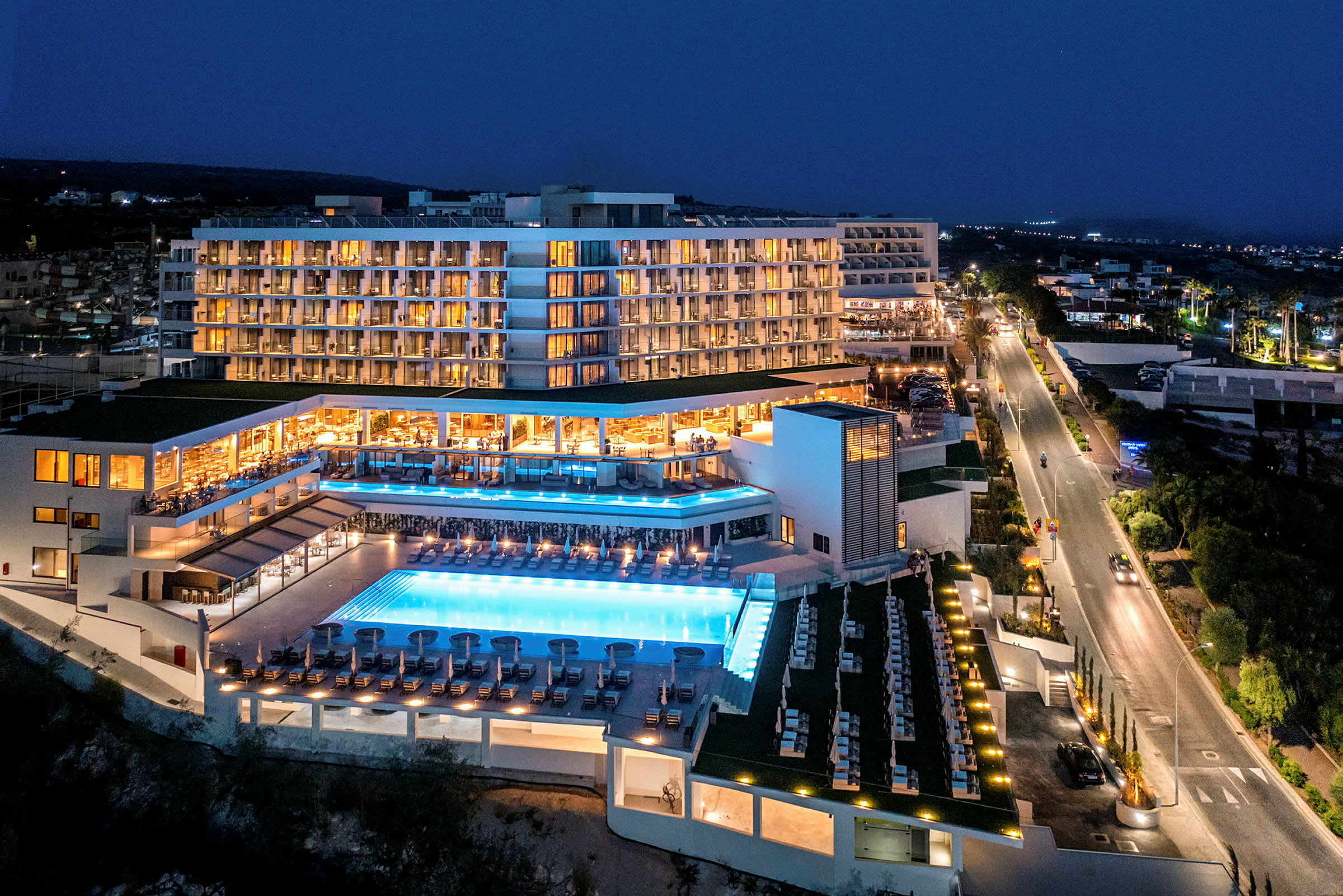 Hotelbygning om aftenen med oplyst poolområde. (AI-genereret tekst)