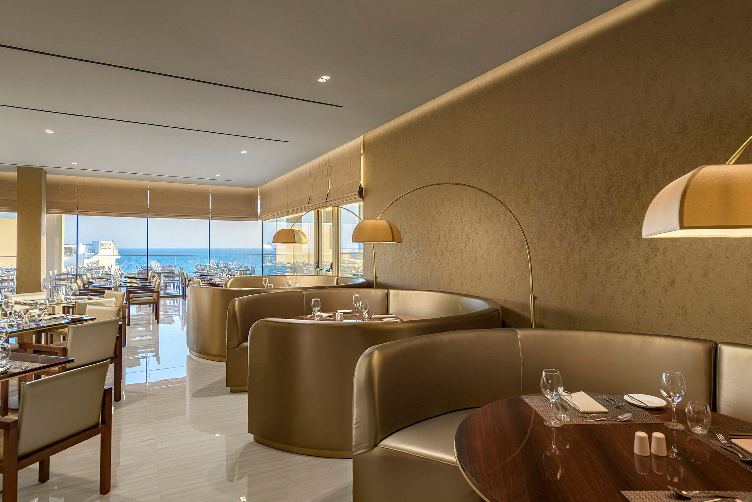 En elegant restaurant med siddegrupper og borde dækket med glas og bestik samt udsigt over havet. (AI-genereret tekst)