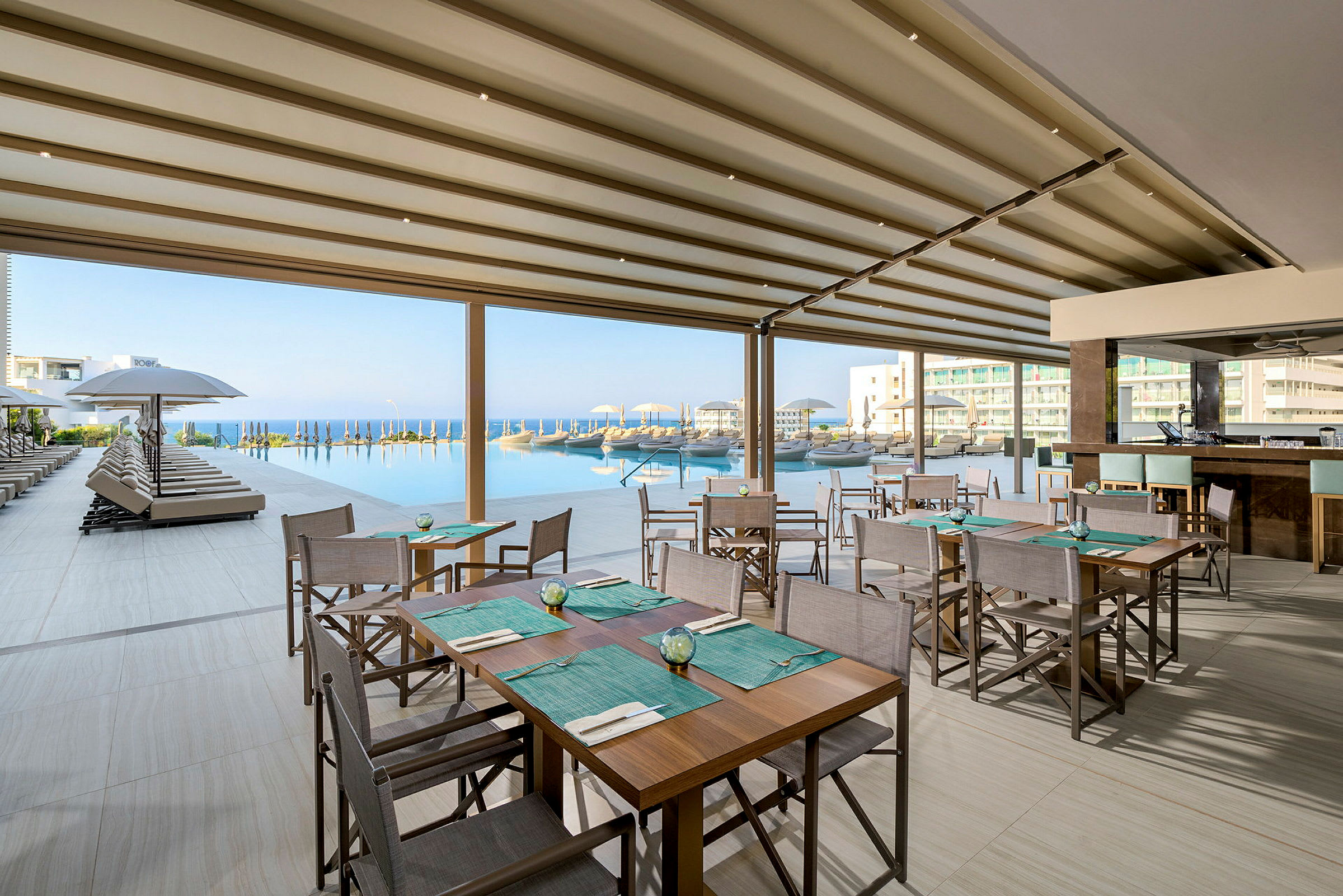 Restaurant med siddepladser ved en pool med udsigt over havet. (AI-genereret tekst)
