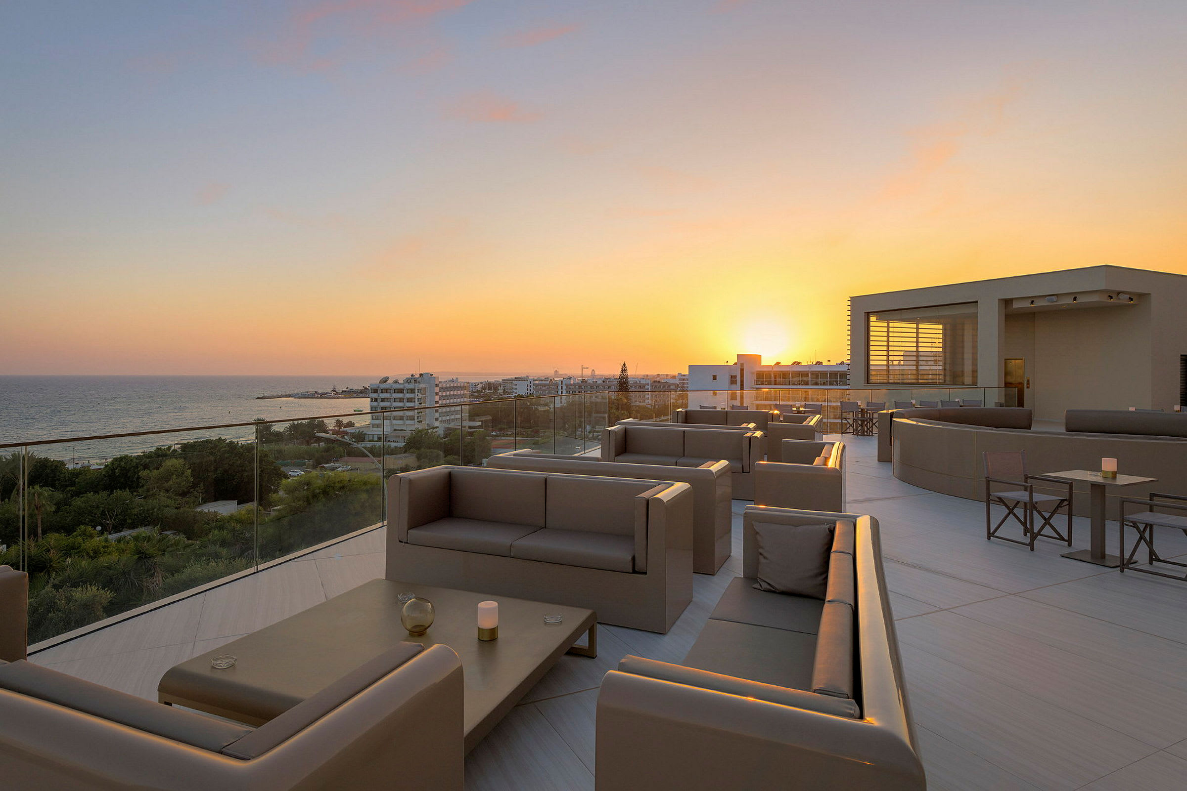 Terrasse med siddepladser og udsigt over solnedgang og hav. (AI-genereret tekst)