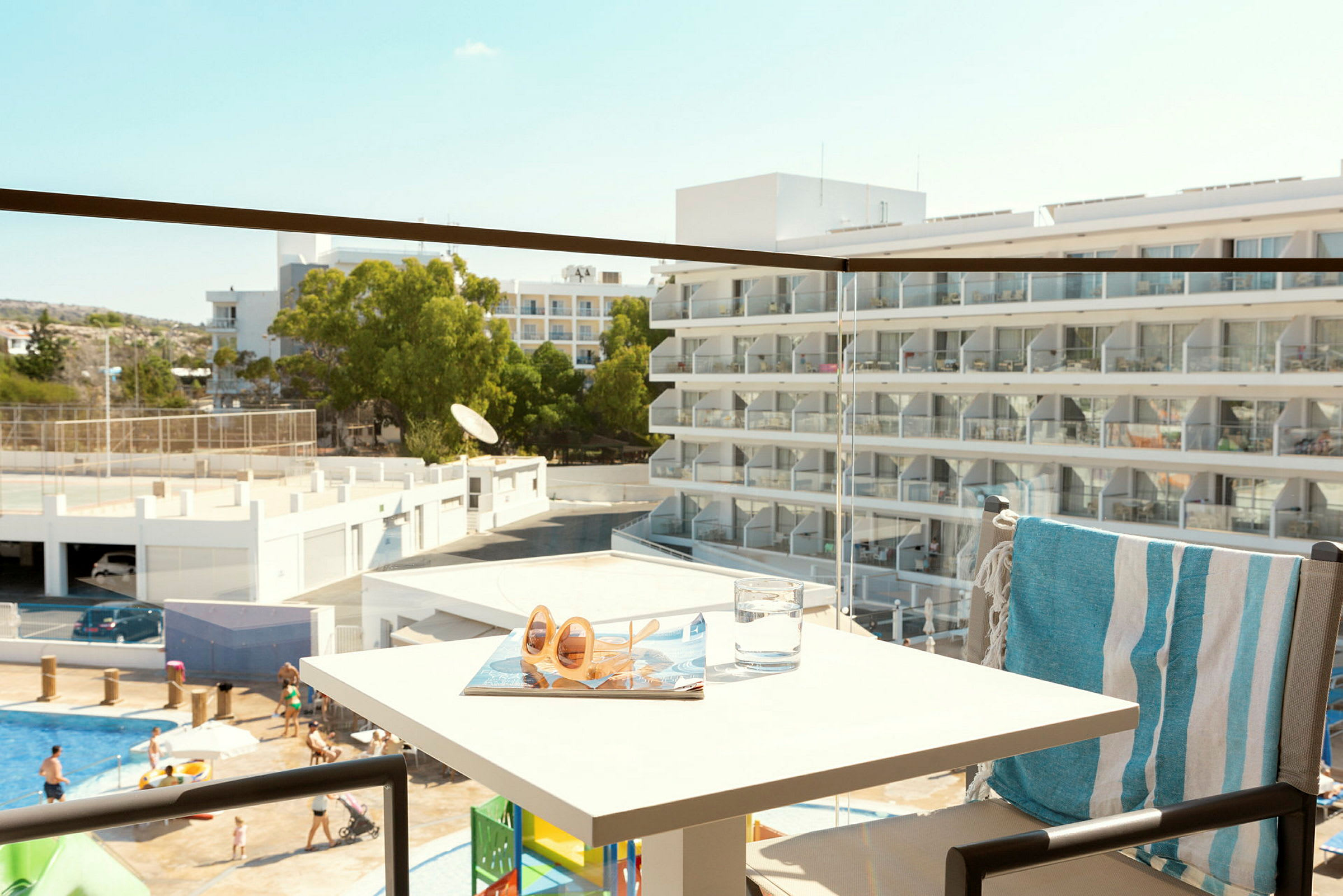 Udsigt fra en altan til en hotelbygning med altaner og mennesker ved en pool. (AI-genereret tekst)