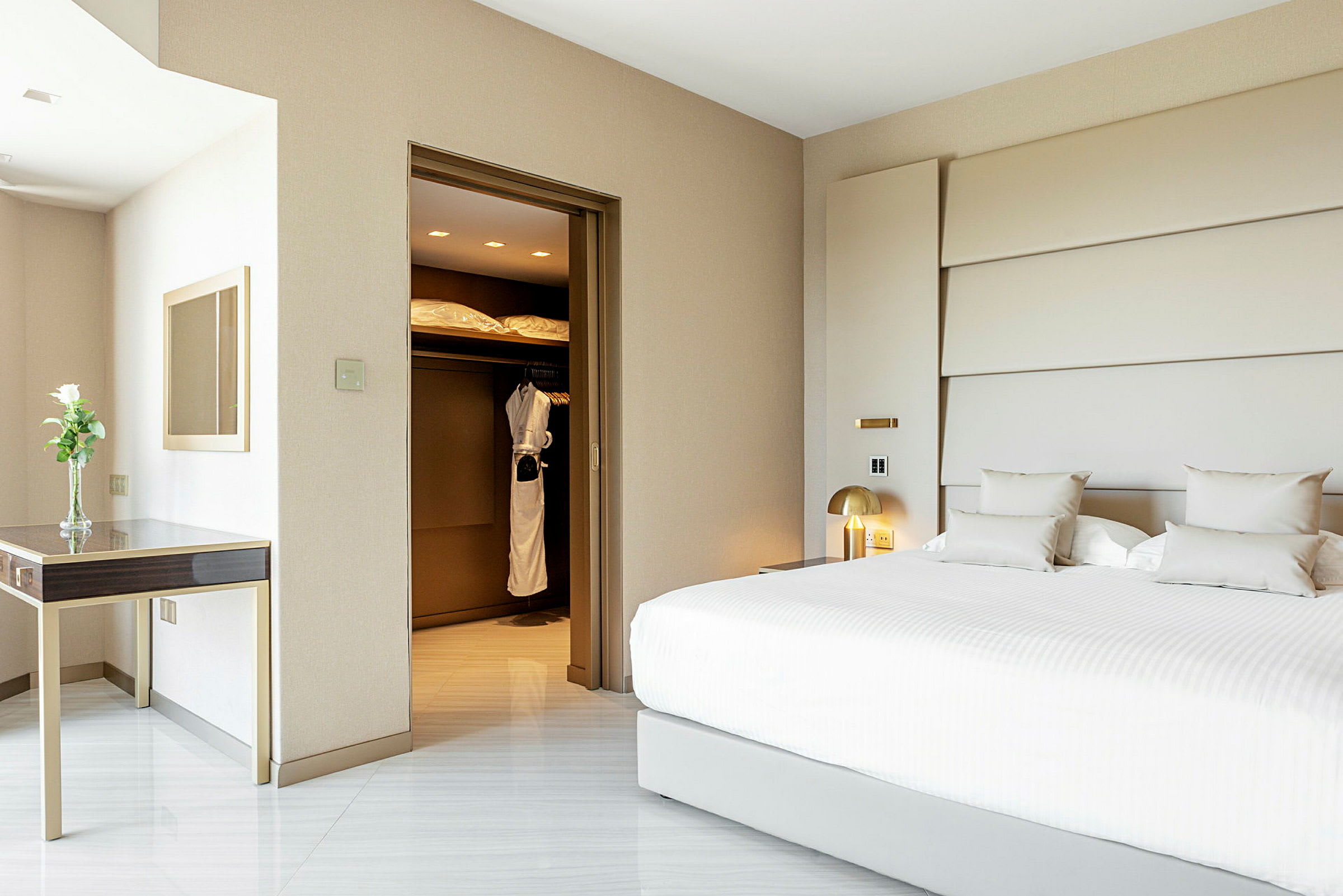 Hotelværelse med en stor hvid seng, et skrivebord med en vase og et skab med morgenkåber. (AI-genereret tekst)