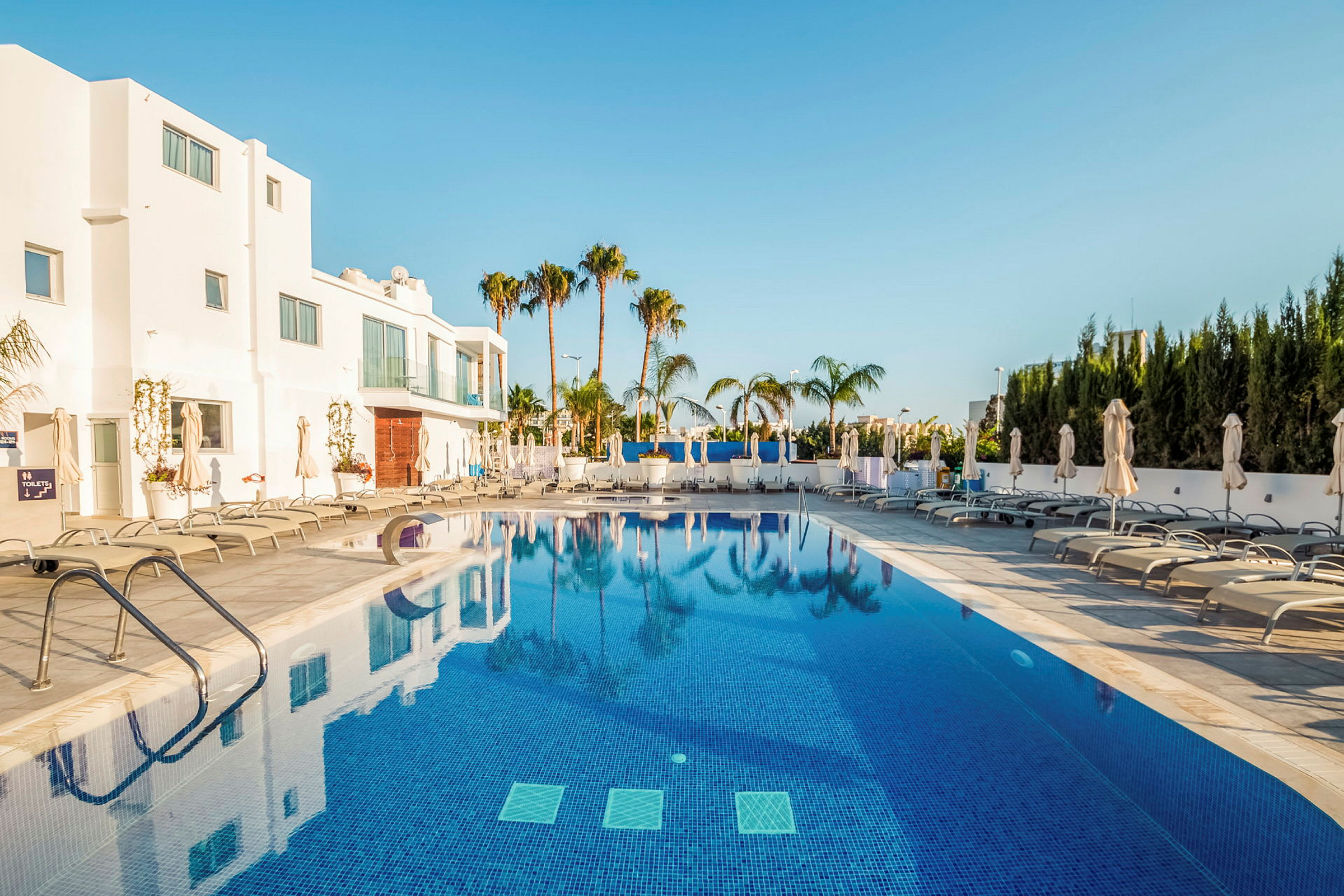 Udendørs pool ved hotel med liggestole og parasoller. (AI-genereret tekst)