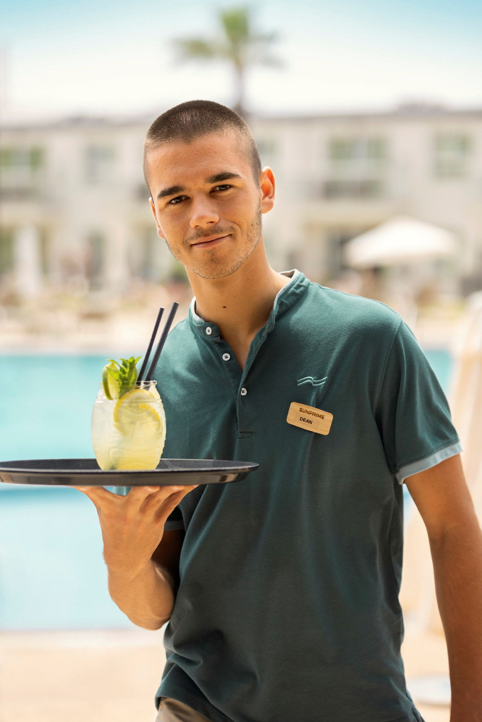 Person i uniform, der bærer en bakke med en drink ved en pool. (AI-genereret tekst)