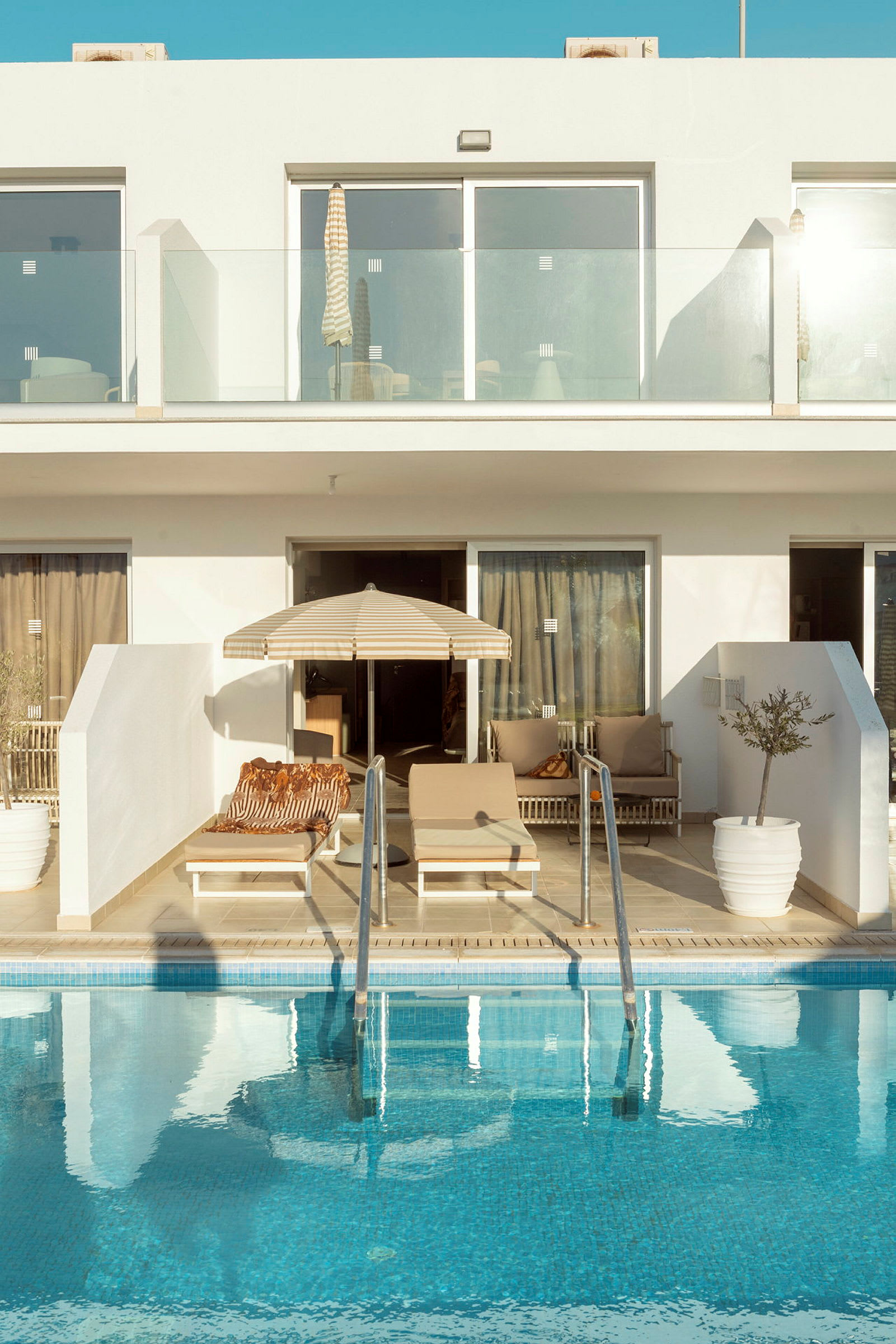 Billede af en moderne feriebolig med private liggestole, parasol og pool. (AI-genereret tekst)