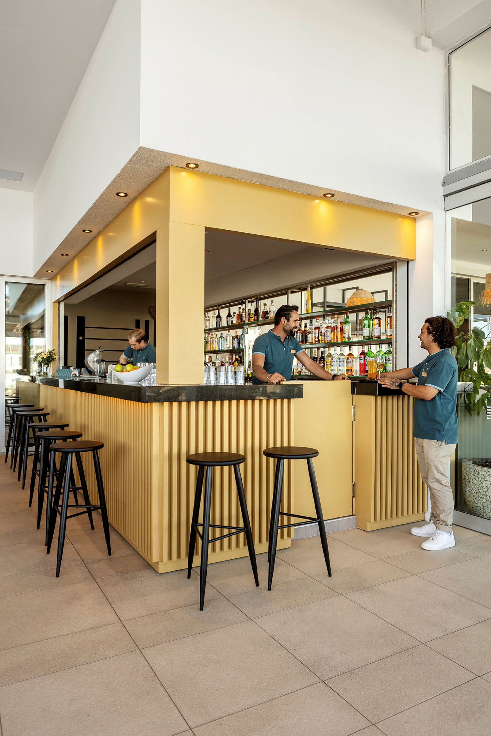 En moderne bar med gul indretning og sorte høje stole. (AI-genereret tekst)