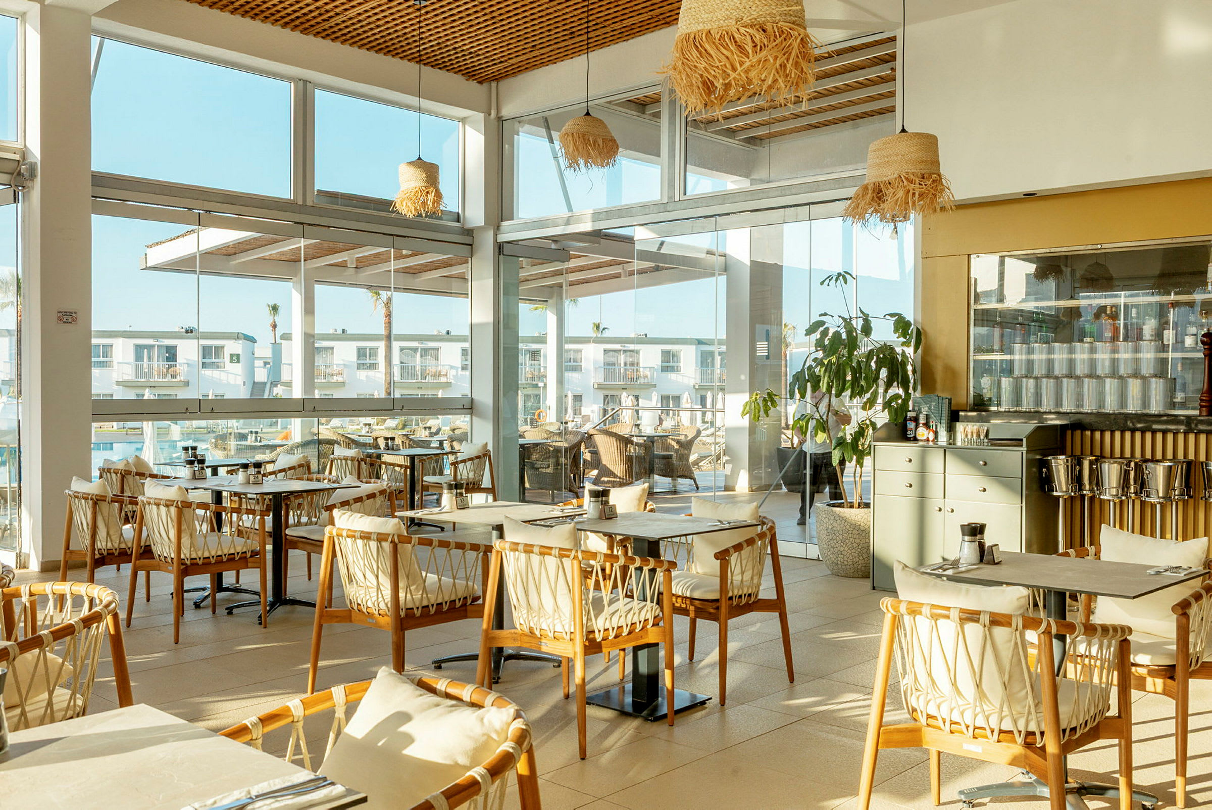En restaurant med store vinduer og træstole omkring bordene. (AI-genereret tekst)