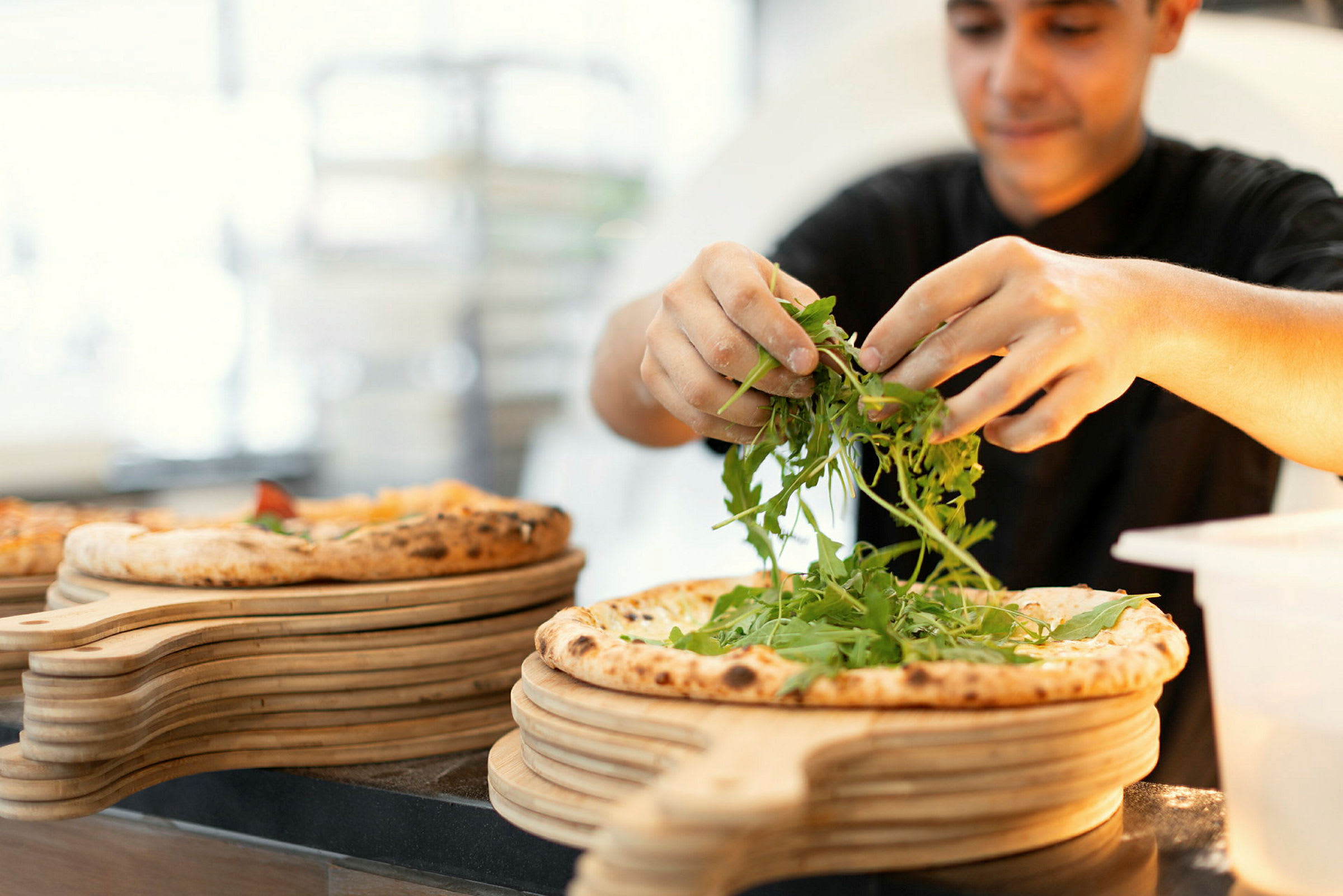 En person dekorerer en pizza med rucolasalat. (AI-genereret tekst)