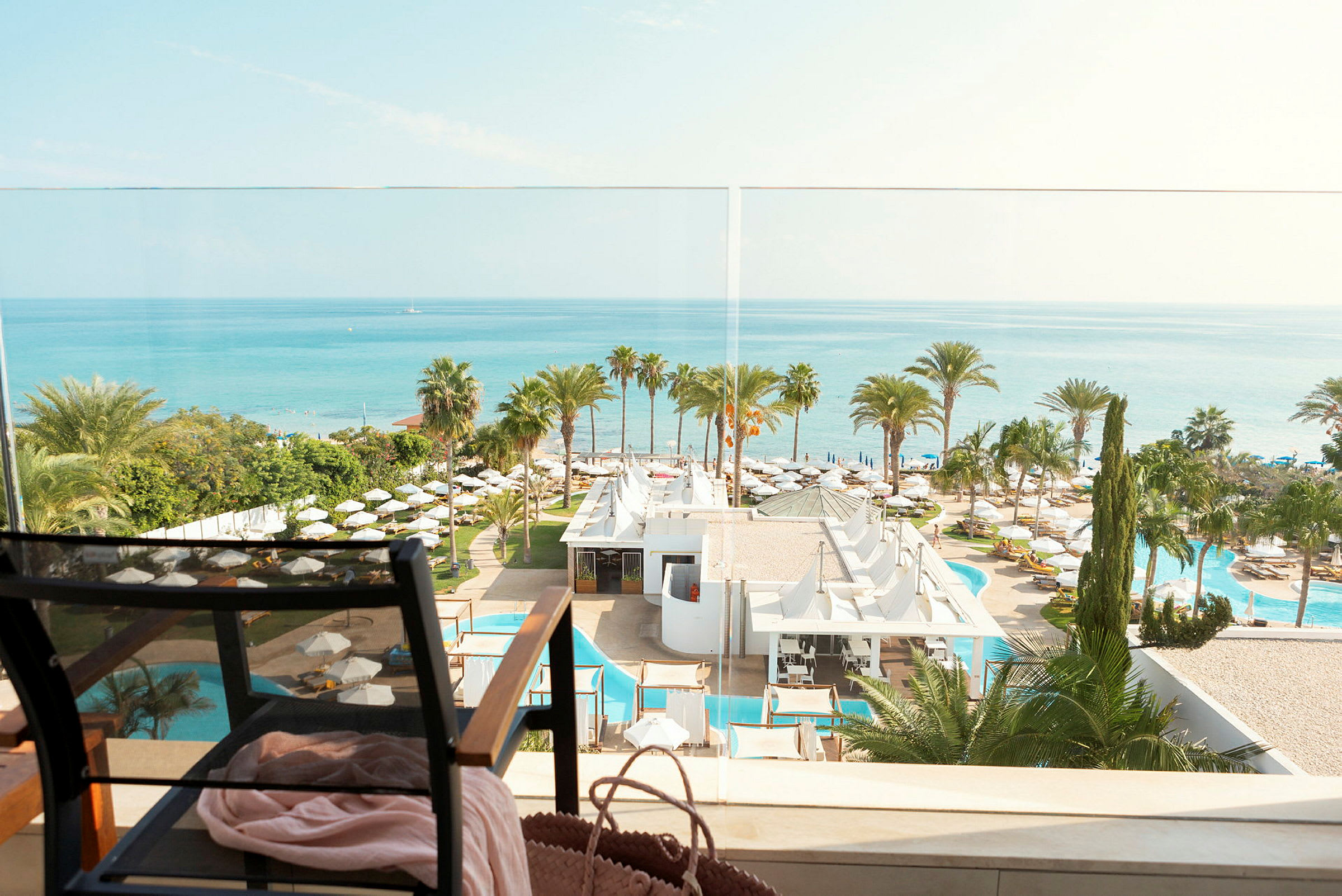 Udsigt over havet, hotelområde med palmer og swimmingpools, og en stol i forgrunden. (AI-genereret tekst)