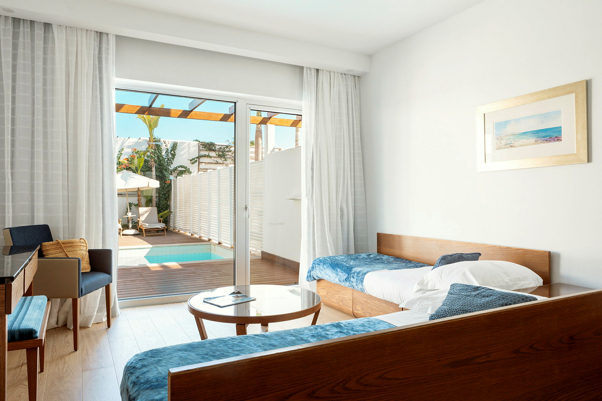 Et hotelværelse med senge, bord og stole, samt en glasdør med udsigt til en terrasse med en lille pool. (AI-genereret tekst)