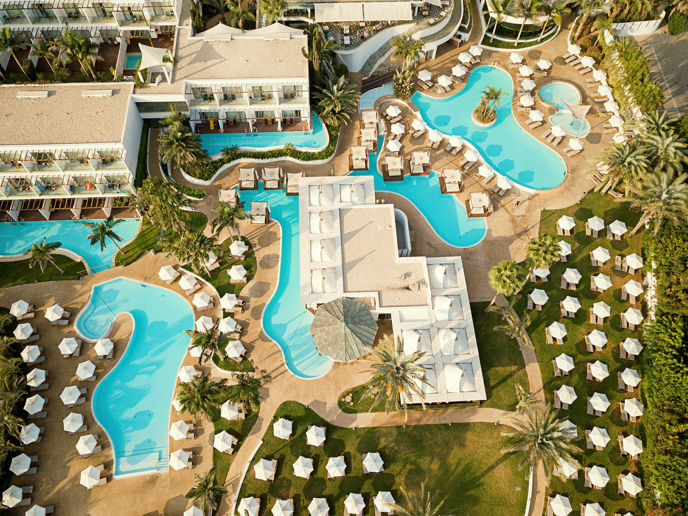 Luftfoto af et hotel med flere swimmingpools og liggestole. (AI-genereret tekst)