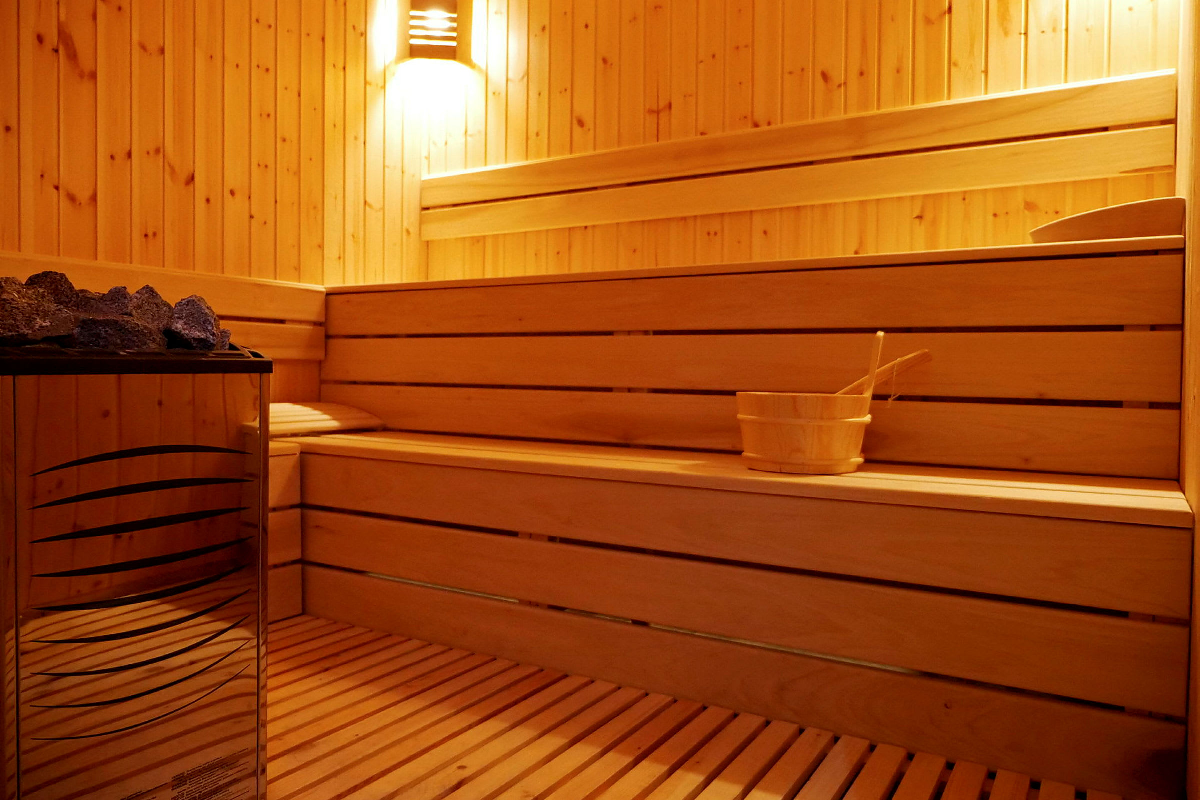 Et sauna-rum med træpaneler, siddepladser og en varmeaggregat samt en skovl. (AI-genereret tekst)