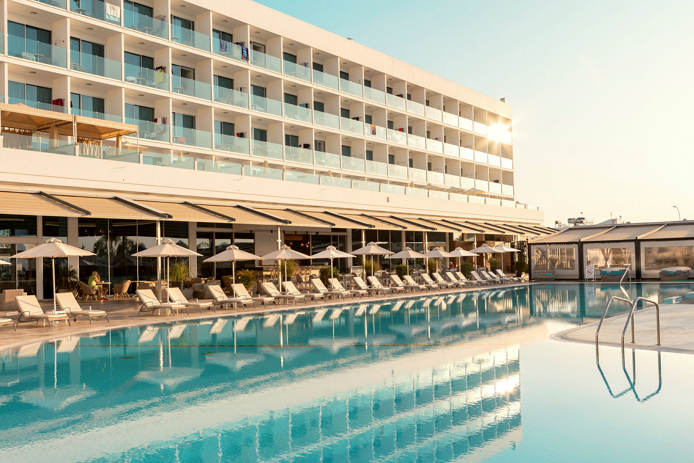 En hotelbygning med altaner ses bag en pool og liggestole. (AI-genereret tekst)