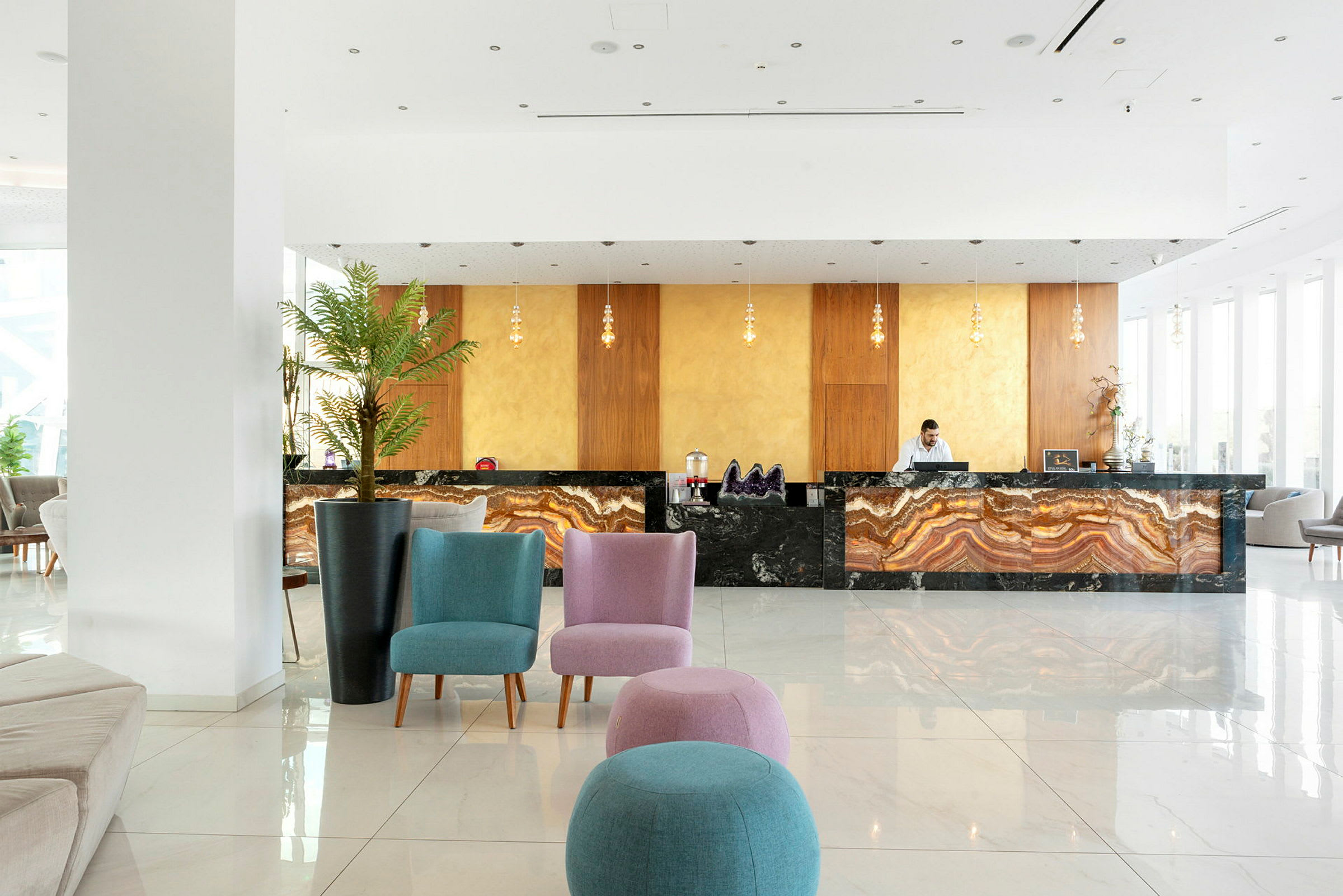 Et hotelreceptionsområde med en marmoreret receptionsdisk, farverige siddepladser og dekorative planter. (AI-genereret tekst)