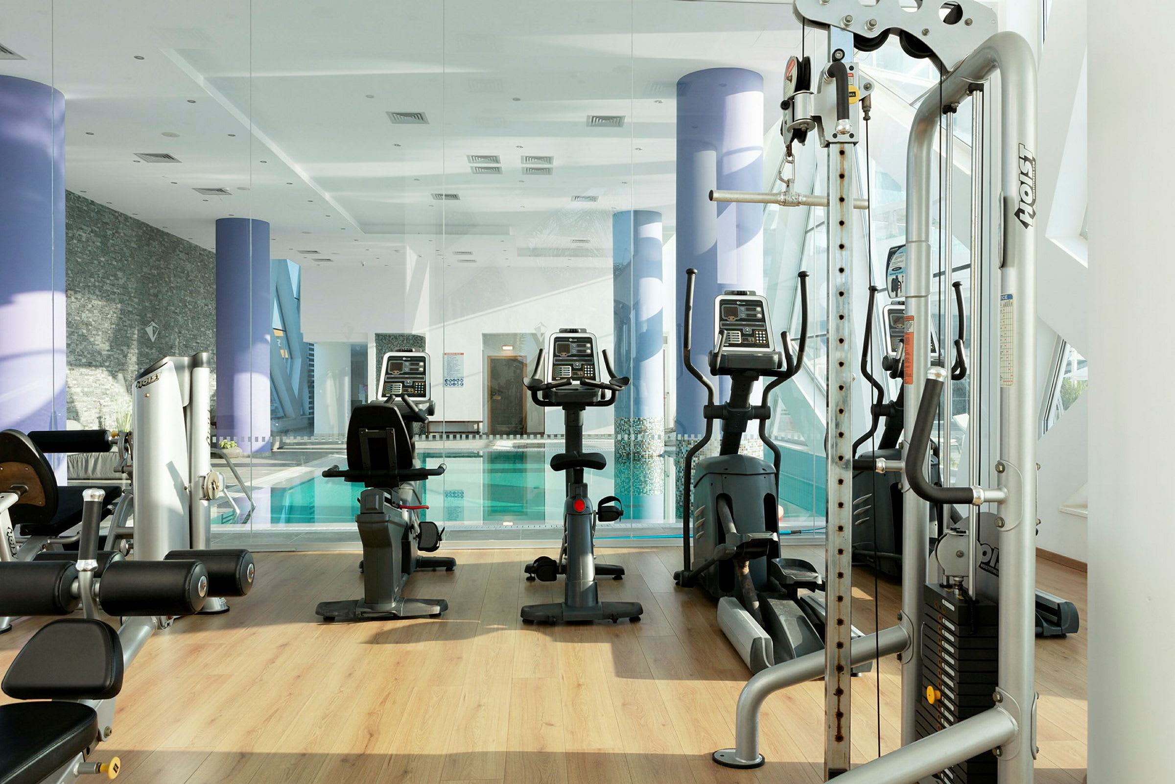 Et fitnesscenter med træningsmaskiner og udsigt til en indendørs pool. (AI-genereret tekst)