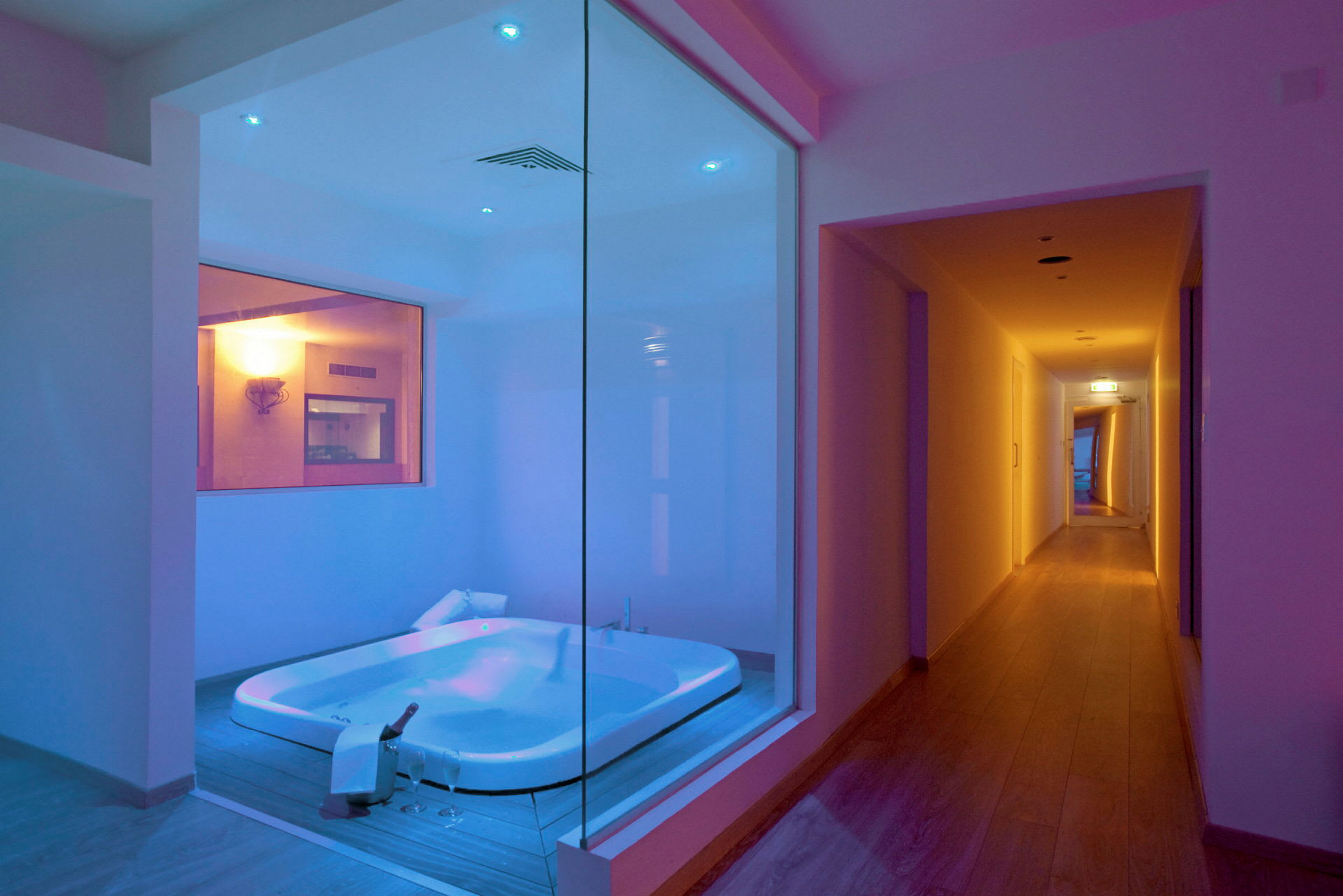 Et moderne badeværelse med en jacuzzi oplyst i blåt og en tilstødende gang. (AI-genereret tekst)
