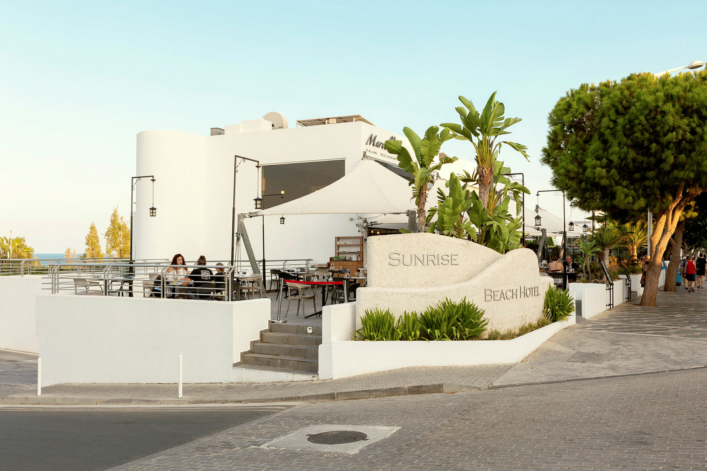 Bygningen og haven ved Sunrise Beach Hotel. (AI-genereret tekst)