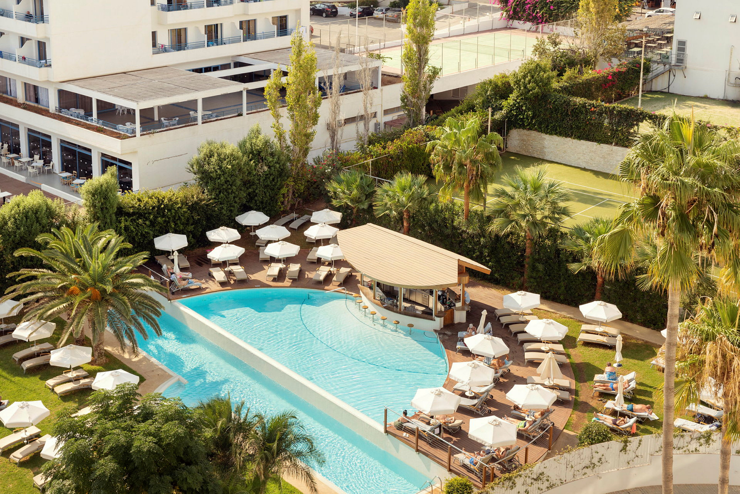 Billede af hotelpoolområde med liggestole, parasoller, palmer og servering. (AI-genereret tekst)