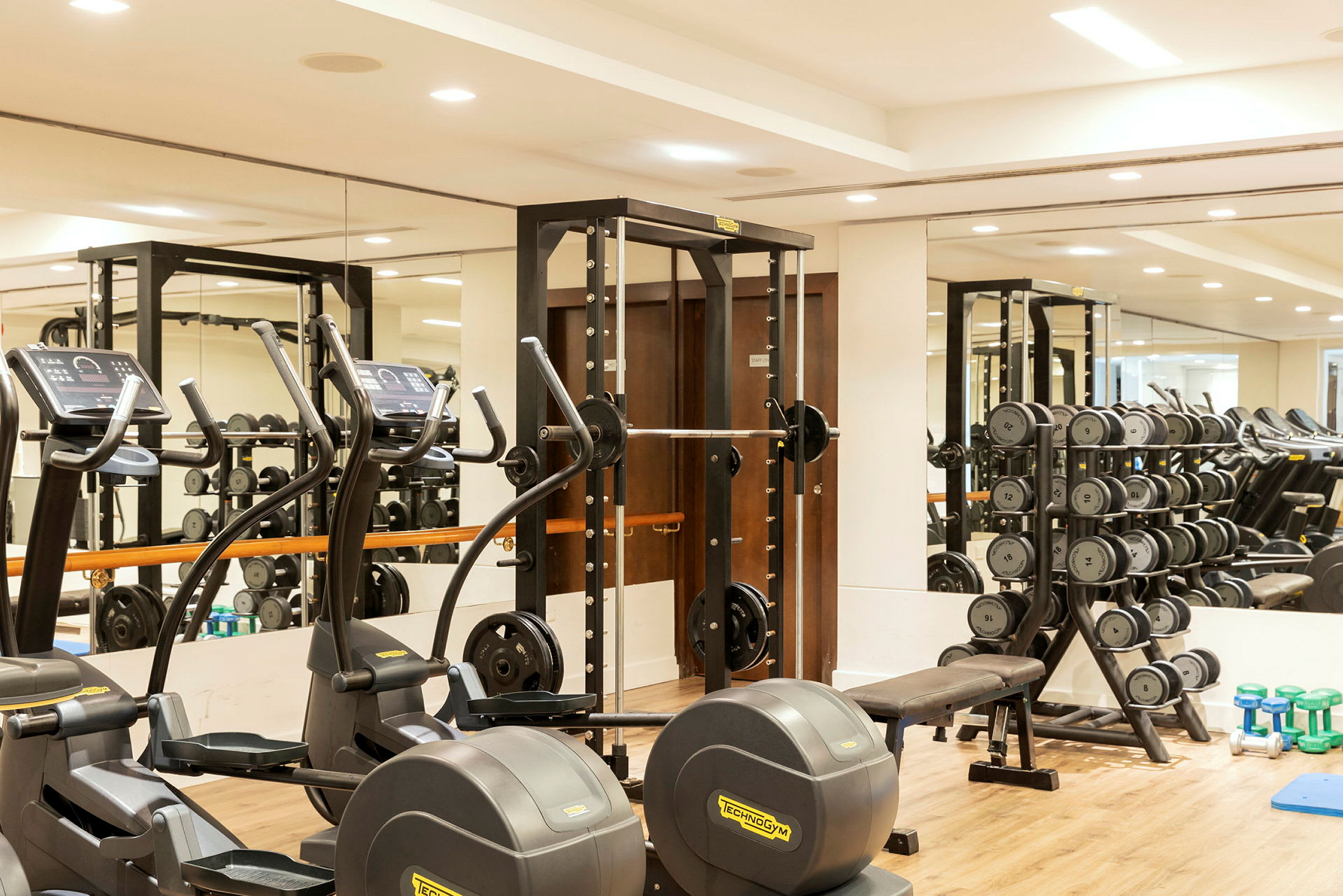 Fitnesscenter med træningsmaskiner, frie vægte og spejlvæg. (AI-genereret tekst)
