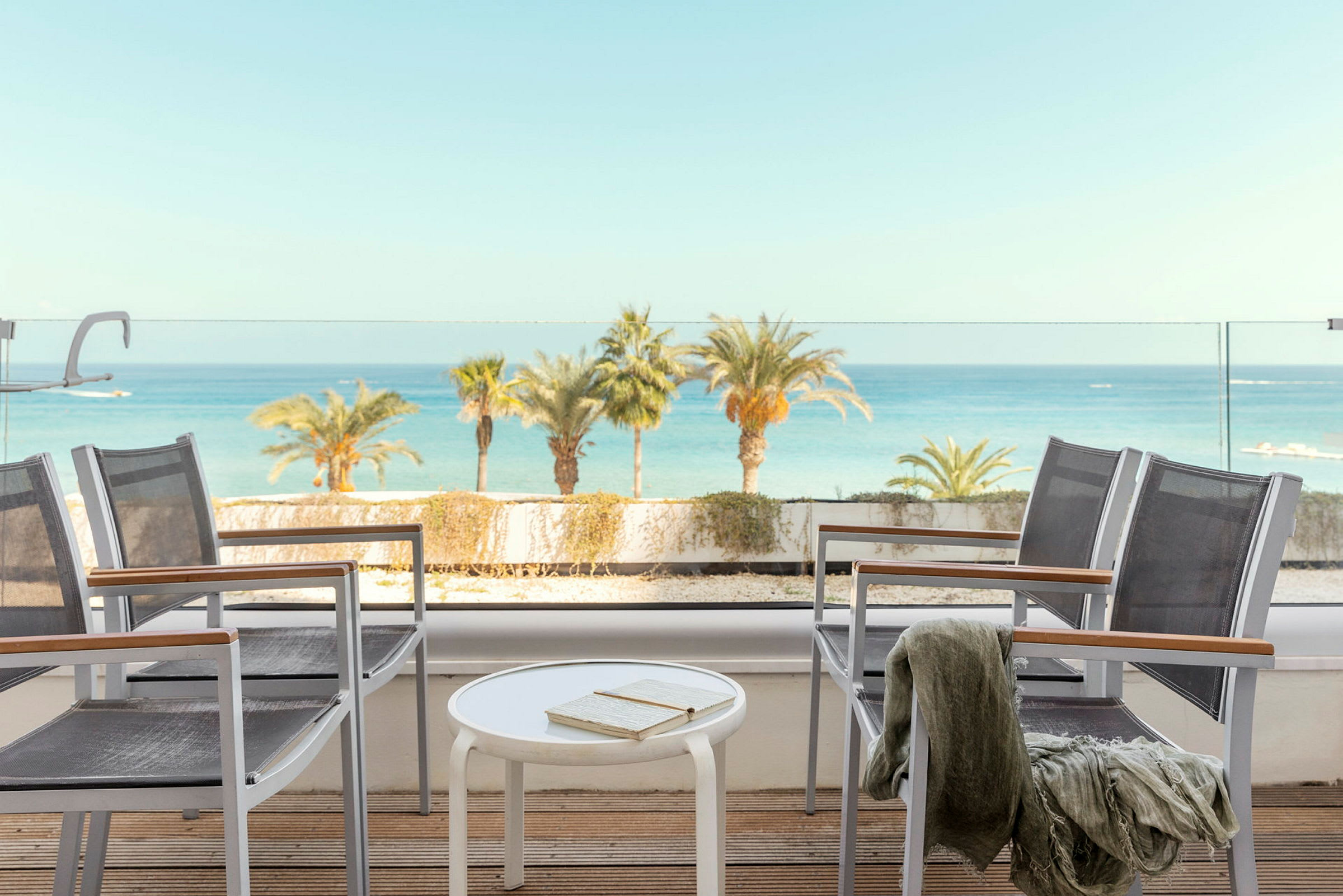 Udsigt fra en terrasse med stole, bord og havet i baggrunden. (AI-genereret tekst)
