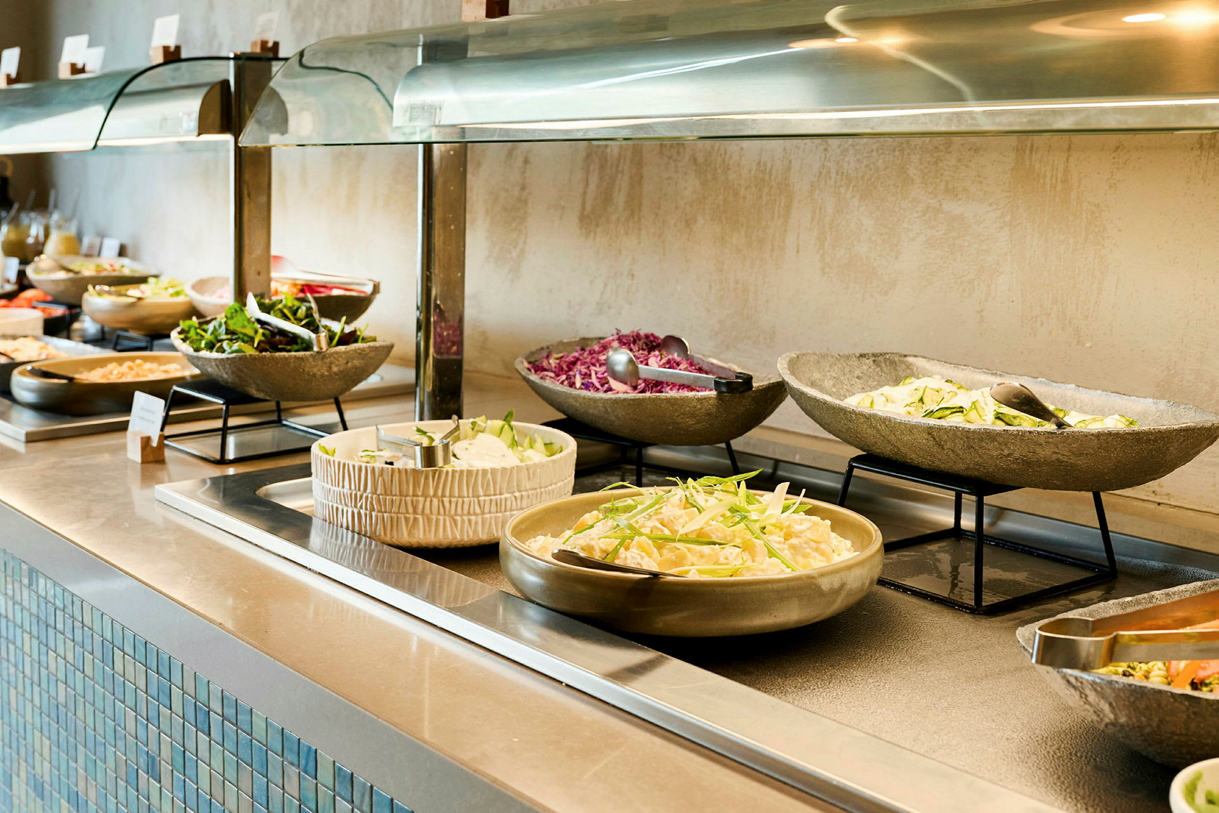 Billede af en buffet med forskellige salater og tilbehør i skåle. (AI-genereret tekst)