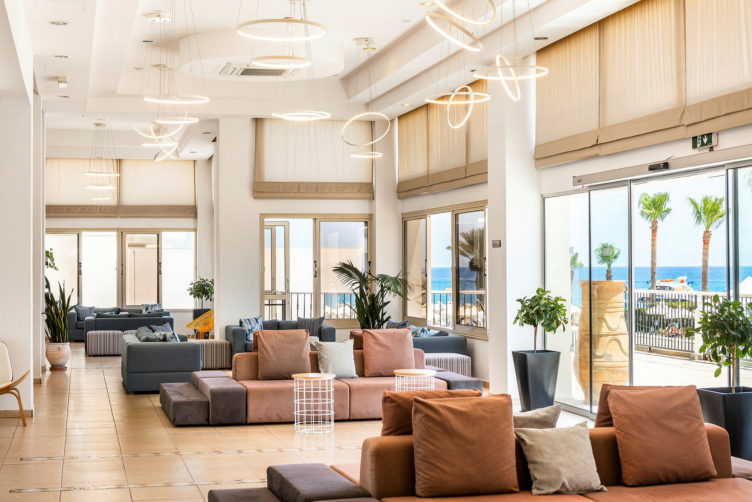 Lys og rummelig loungedel med moderne sofaer, store vinduer og udsigt til havet. (AI-genereret tekst)
