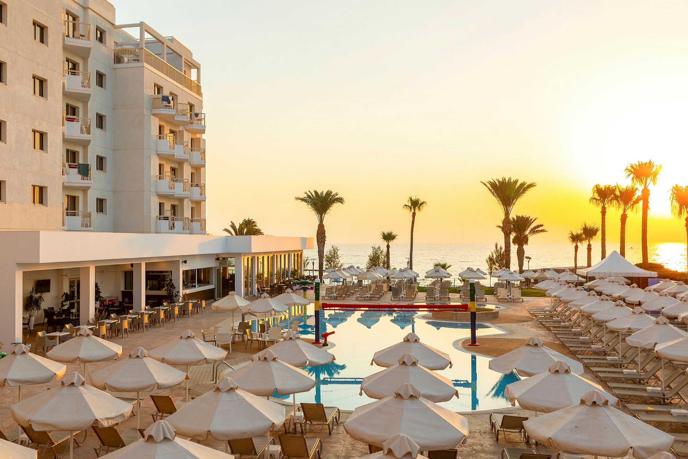 Hotelområde med pool, liggestole og parasoller nær havet ved solnedgang. (AI-genereret tekst)