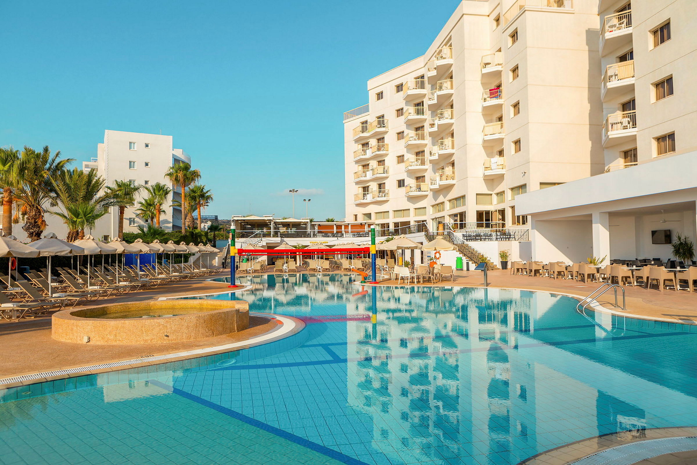 Hotelbygning ved en pool med liggestole og parasoller. (AI-genereret tekst)