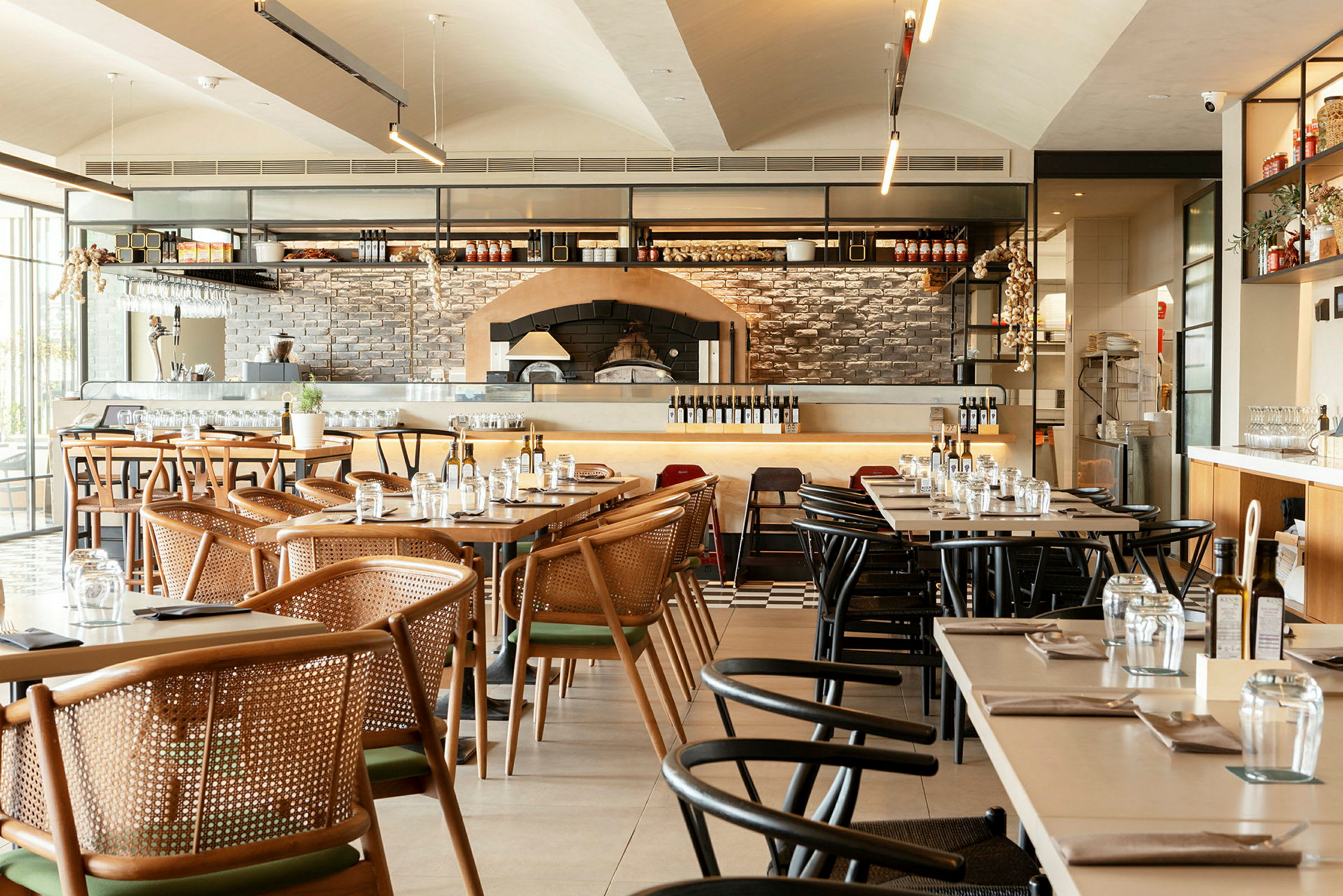 En restaurant med dækkede borde og stole samt synlig pizzaovn. (AI-genereret tekst)
