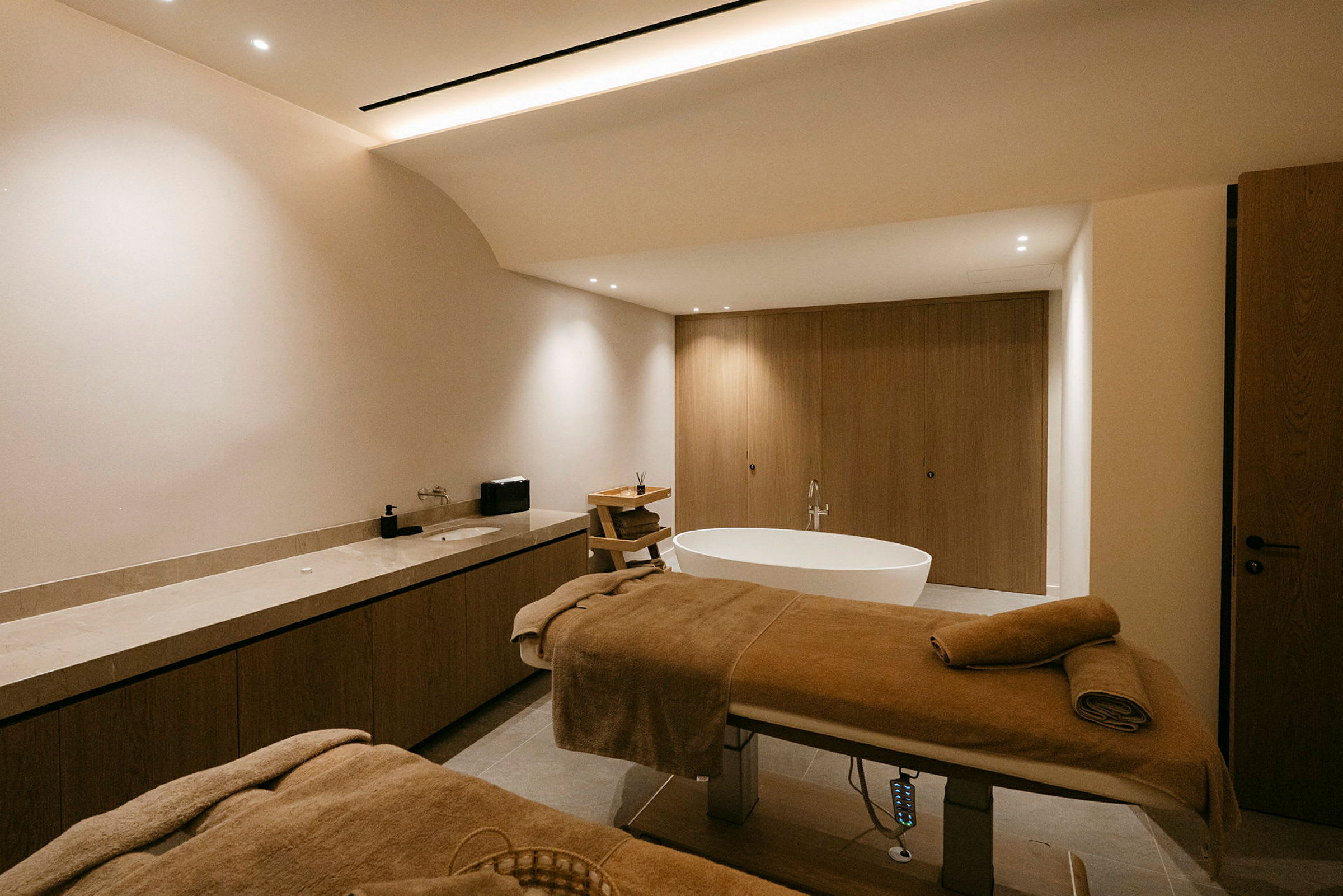Et moderne spa-rum med to massagebænke, et fritstående badekar og træinteriør. (AI-genereret tekst)
