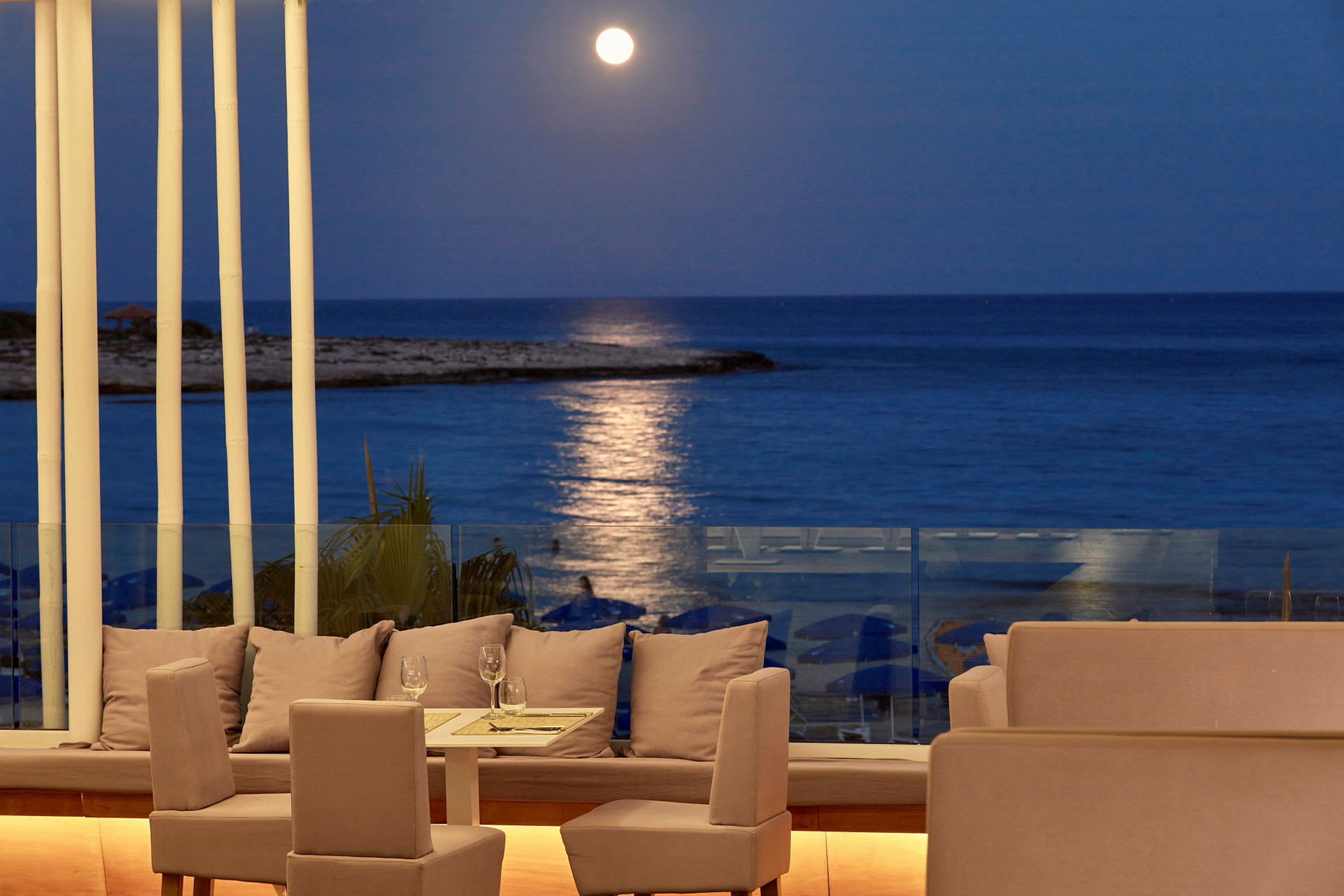 En terrasse med siddepladser og et bord, med udsigt over havet under en klar månebelyst aften. (AI-genereret tekst)