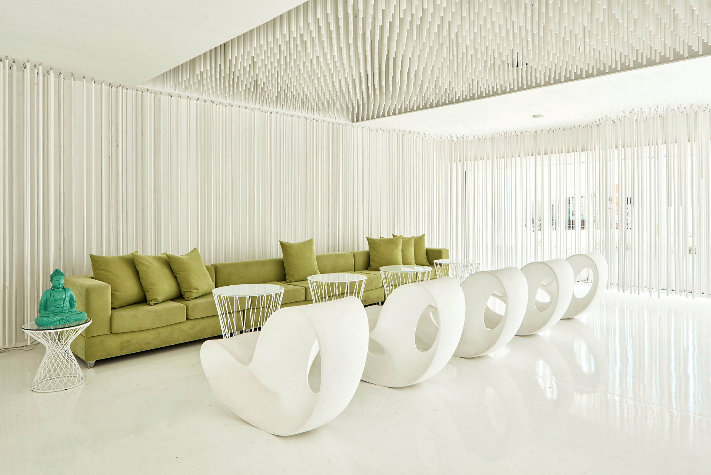 En moderne lounge med grøn sofa, hvide stole og et bord med en turkis Buddha-figur. (AI-genereret tekst)