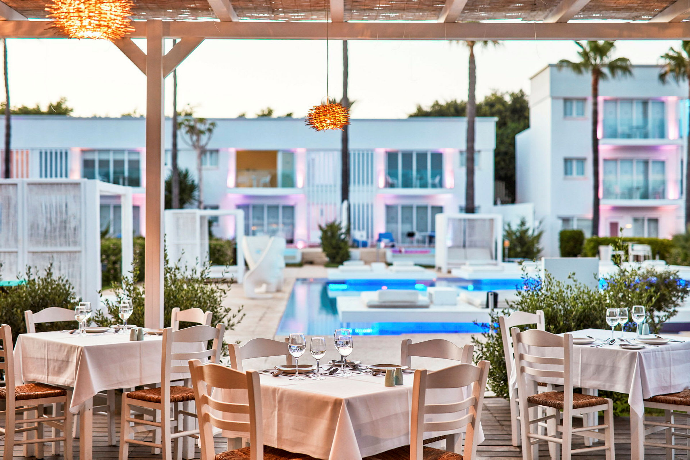 Restaurant med draperede borde ved poolen med moderne bygninger i baggrunden. (AI-genereret tekst)