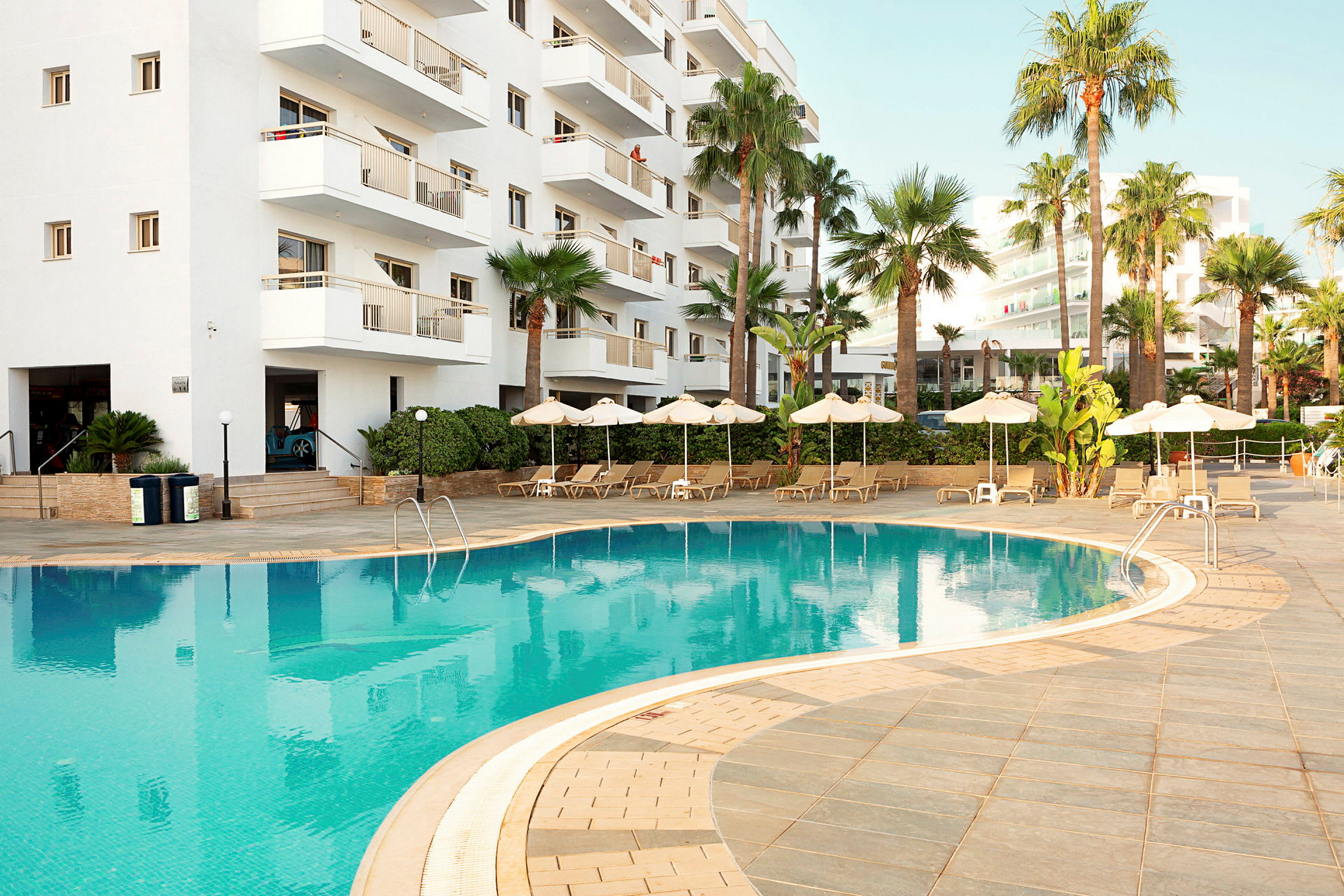 Udendørspool ved hotel med hvid facade. (AI-genereret tekst)