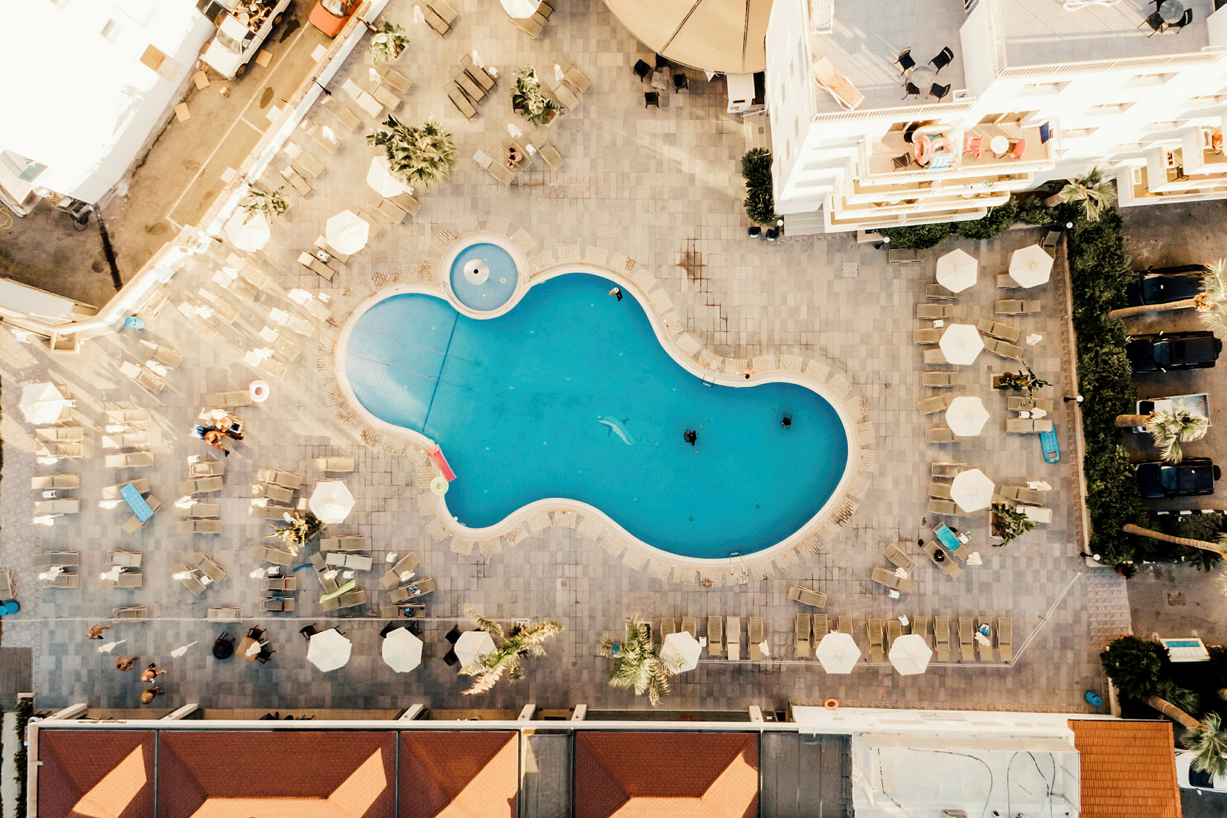 Luftfoto af en fritformet swimmingpool omgivet af liggestole og parasoller. (AI-genereret tekst)