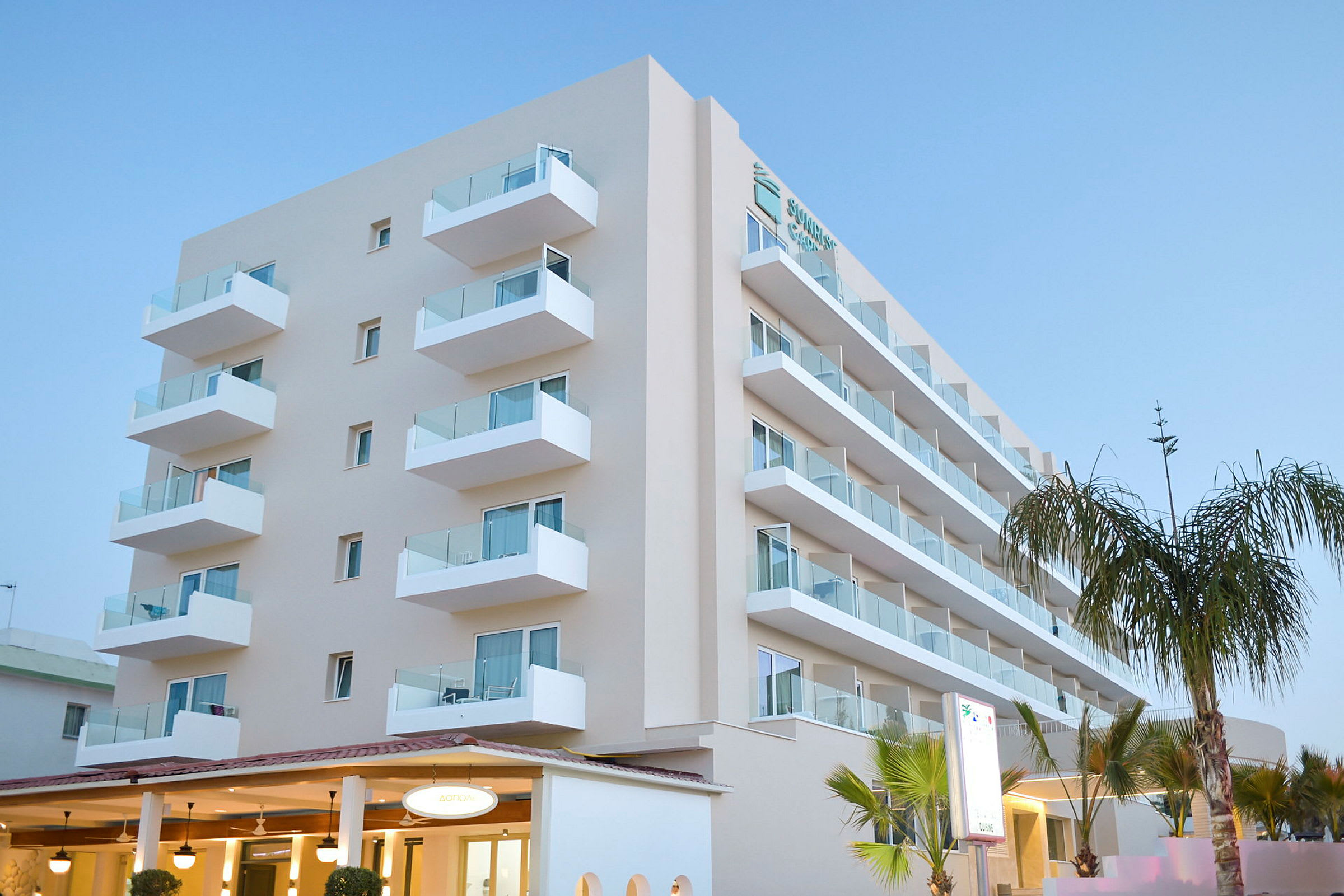 Et moderne hotel med flere etager og altaner, omgivet af palmer. (AI-genereret tekst)