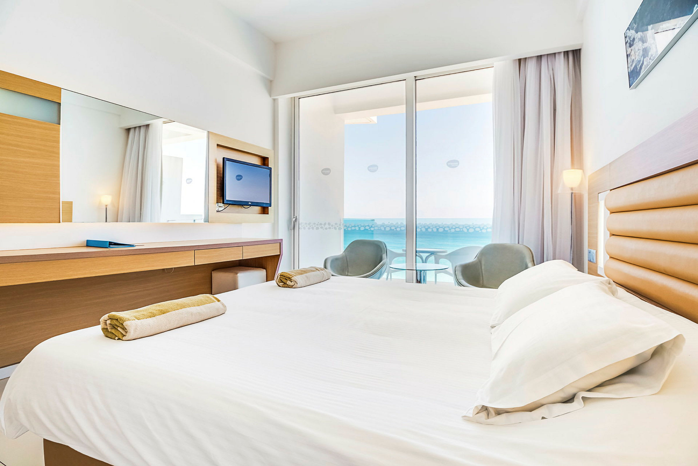 Hotelværelse med seng, skrivebord og balkon med udsigt over havet. (AI-genereret tekst)